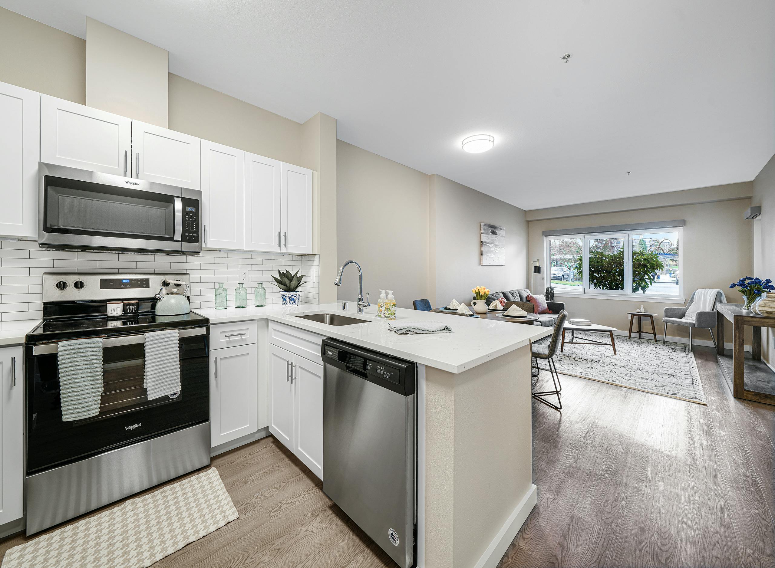Interior of a AMLI Bellevue Park apartment kitchen with stainless steel appliances and white cabinets and view of living room
