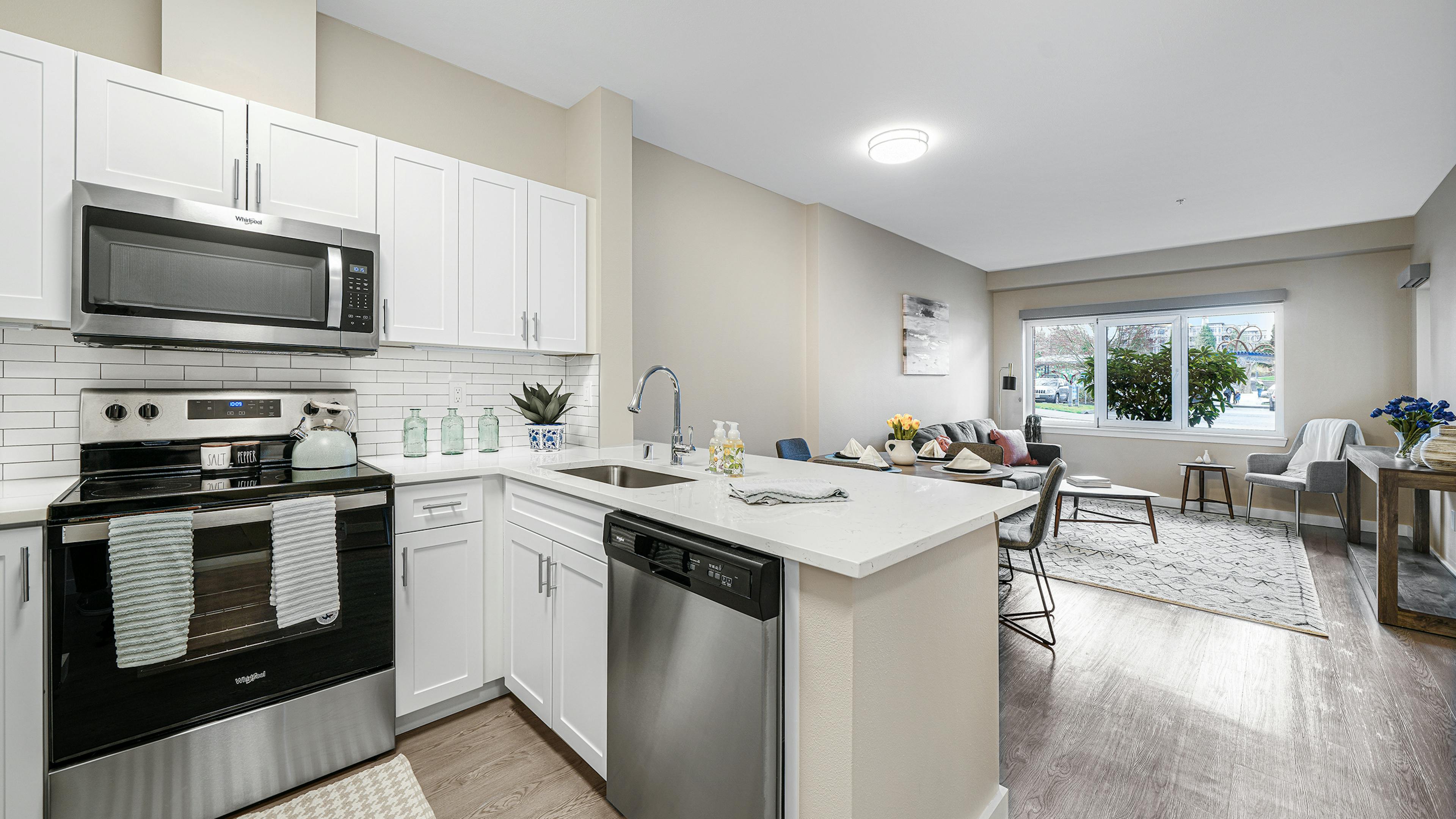 Interior of a AMLI Bellevue Park apartment kitchen with stainless steel appliances and white cabinets and view of living room 