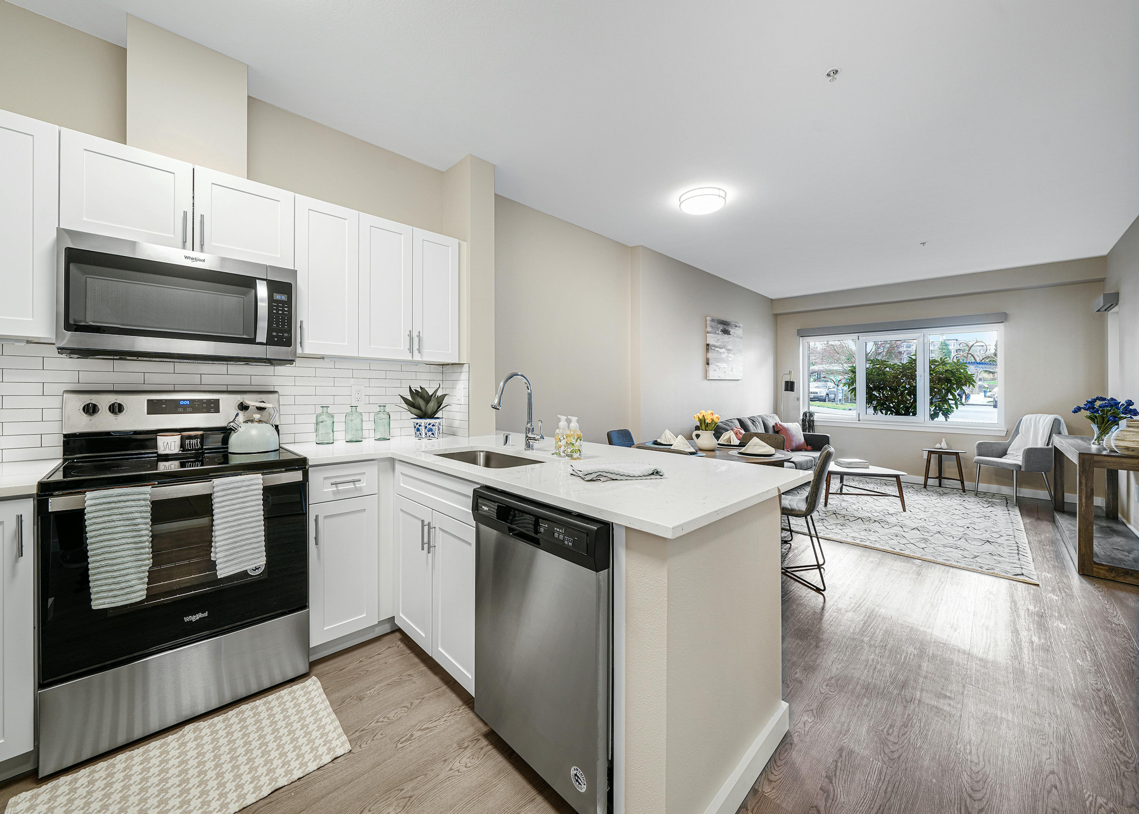 Interior of a AMLI Bellevue Park apartment kitchen with stainless steel appliances and white cabinets and view of living room 