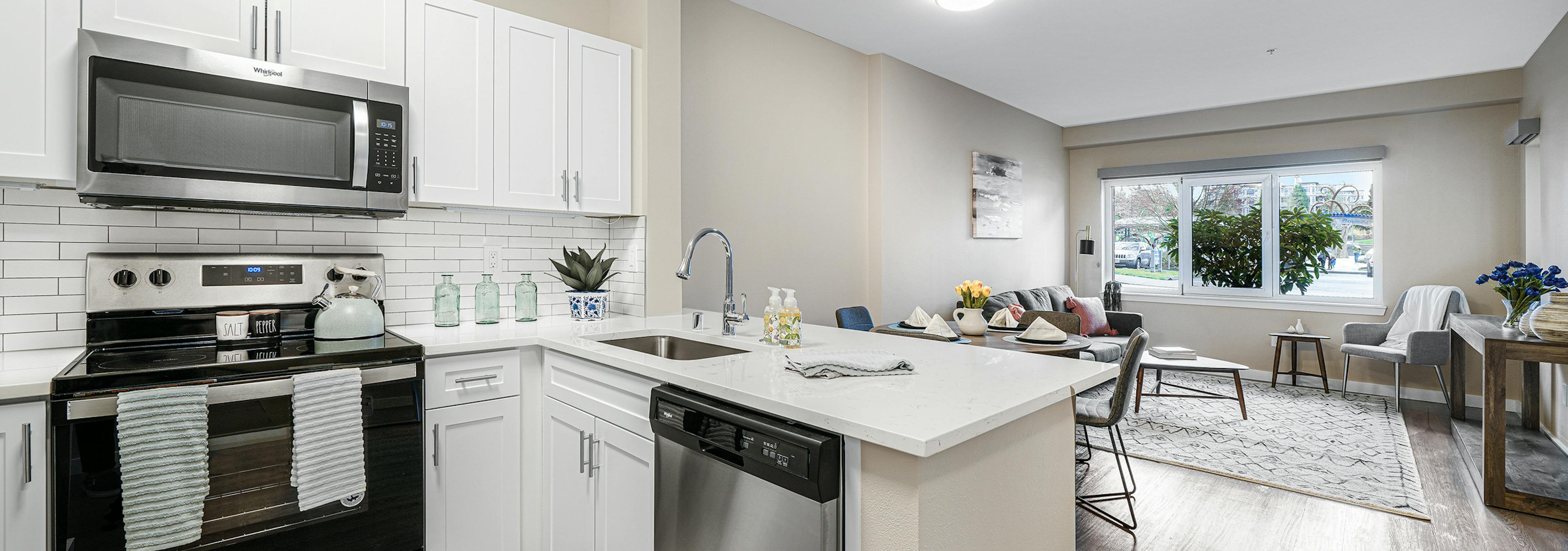 Interior of a AMLI Bellevue Park apartment kitchen with stainless steel appliances and white cabinets and view of living room 