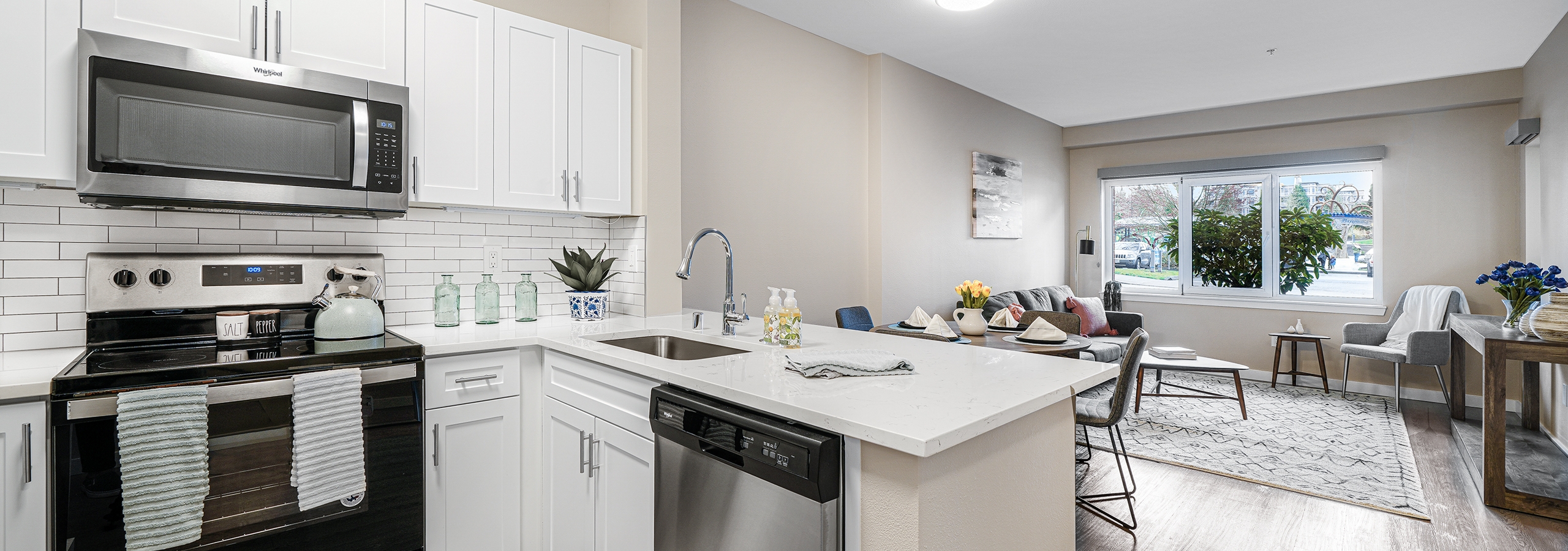 Interior of a AMLI Bellevue Park apartment kitchen with stainless steel appliances and white cabinets and view of living room
