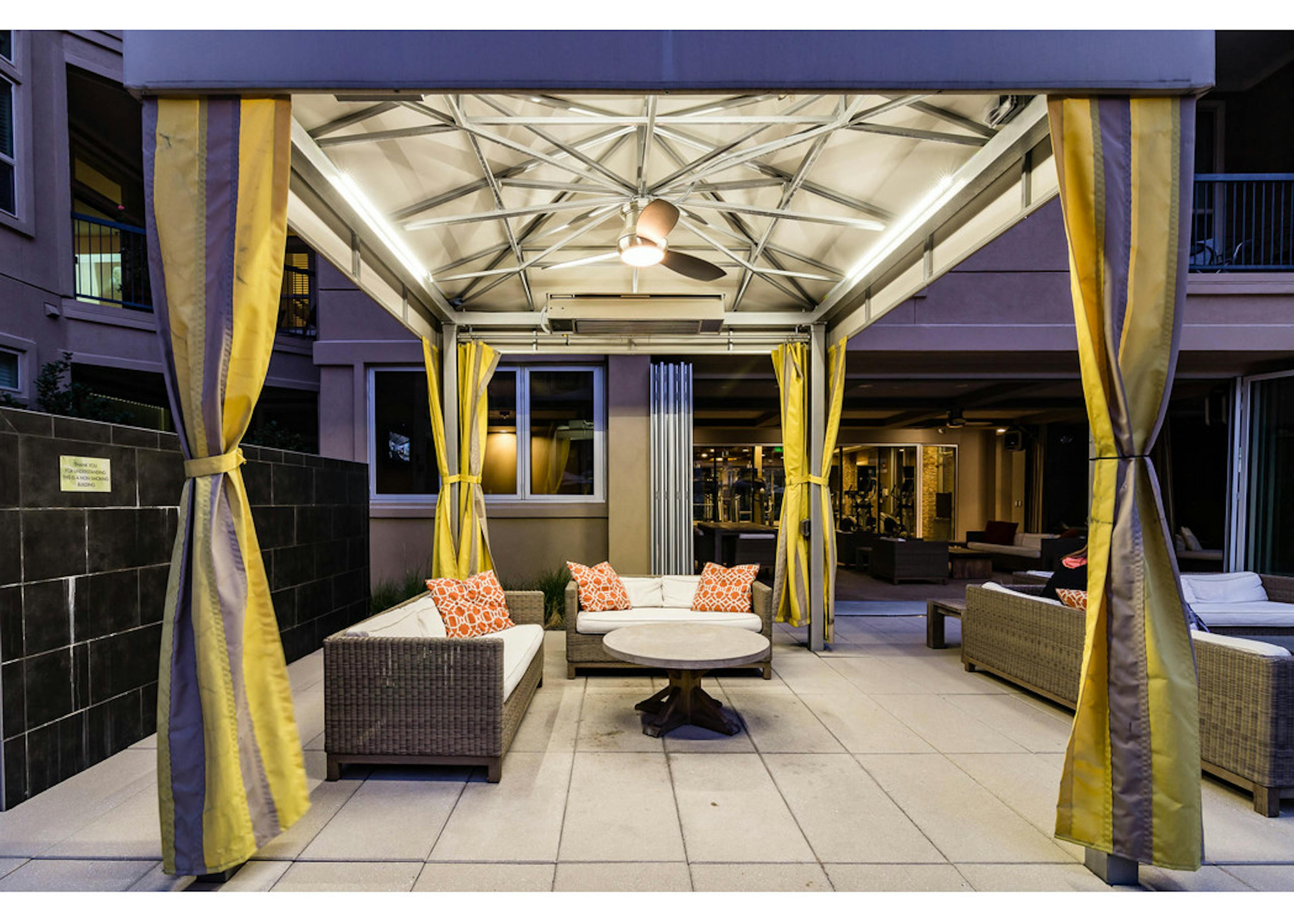 A nighttime view of poolside cabanas at AMLI Ridgegate apartments with Wi-Fi and fire table as well as couches with pillows