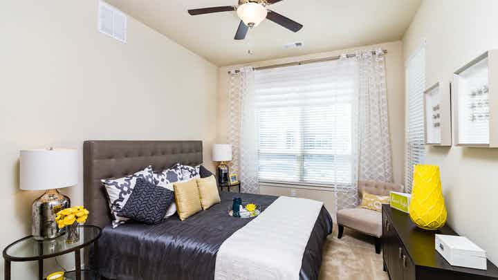 Interior view of AMLI RidgeGate bedroom with queen bed and gray upholstered headboard facing large window with sheer curtains