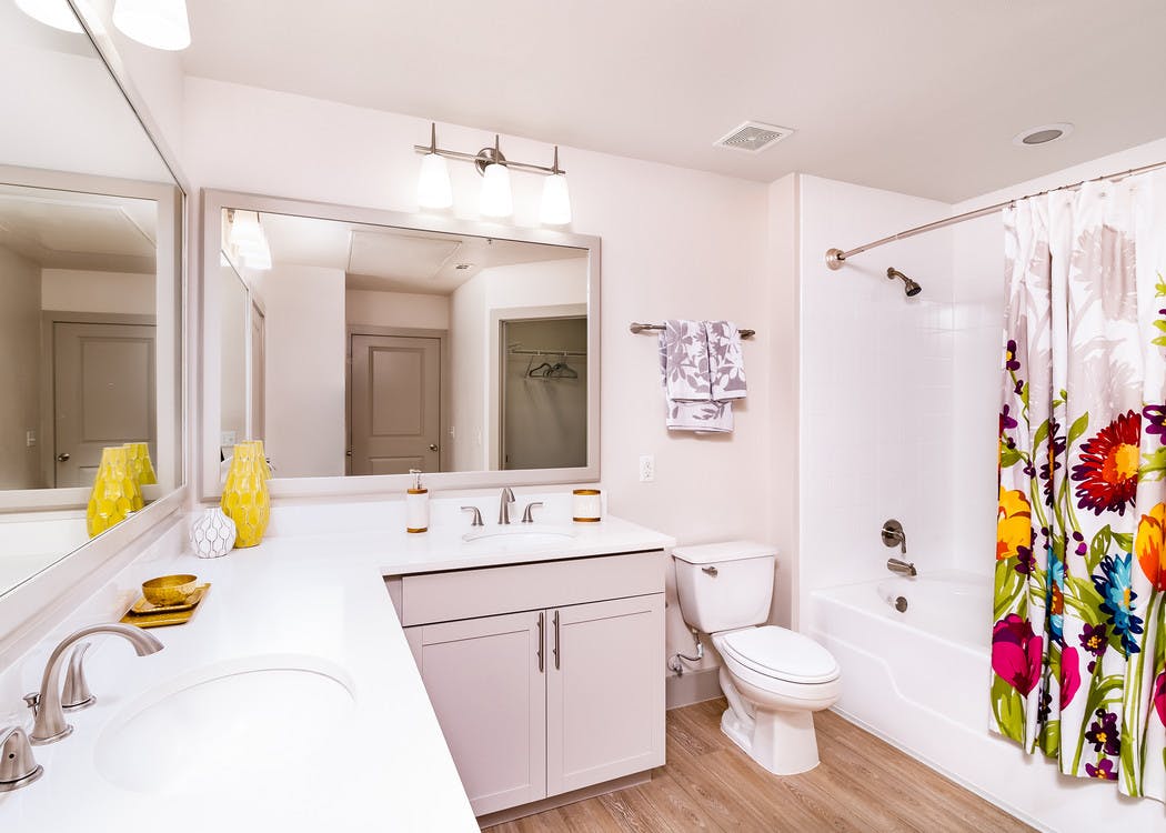 A bathroom at AMLI Park Avenue apartments with white counter tops and two sinks and mirrors with a colorful shower curtain