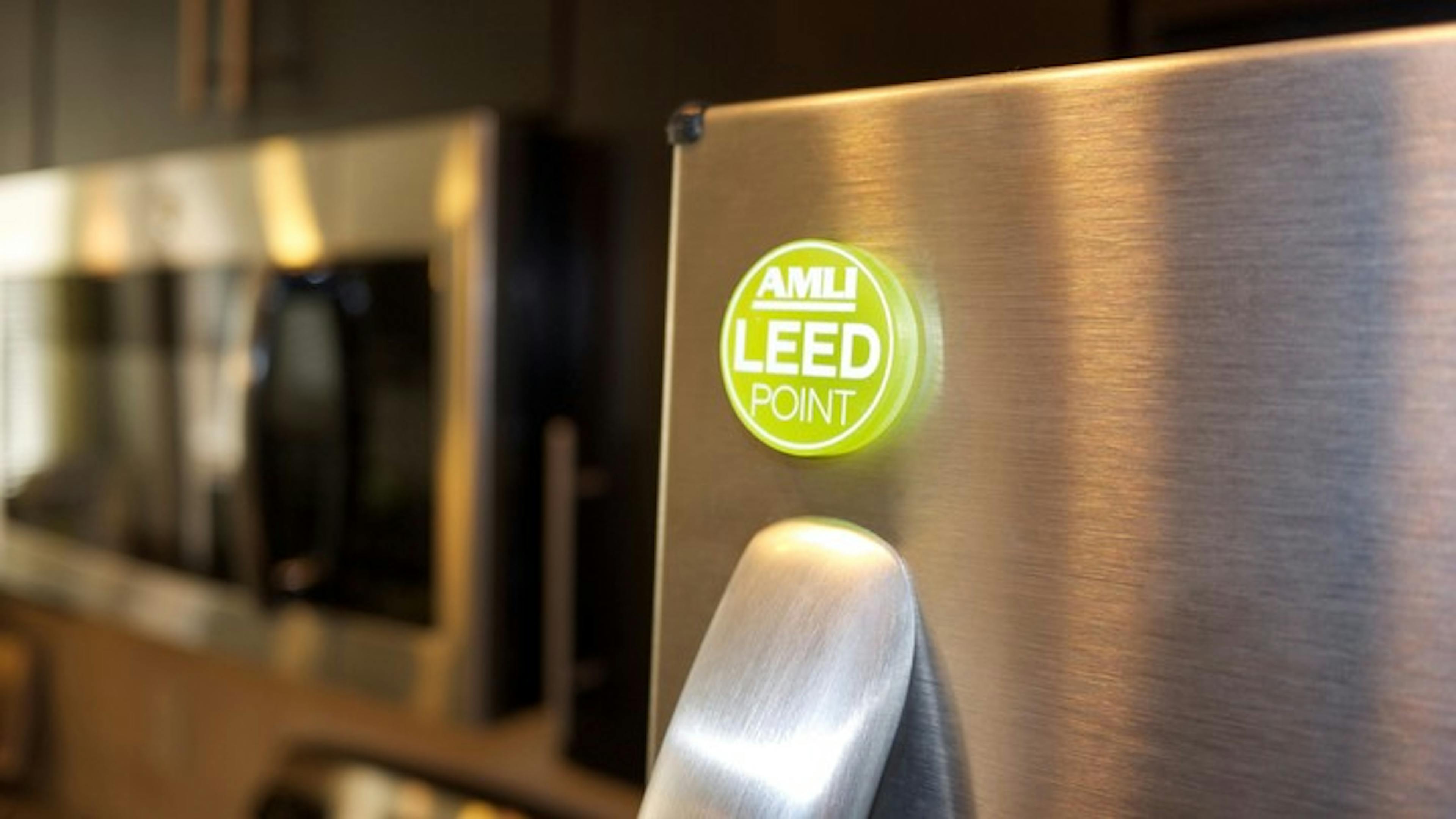 Green magnet saying "AMLI LEED Point" above the handle of a steel energy appliance in the kitchen of an apartment