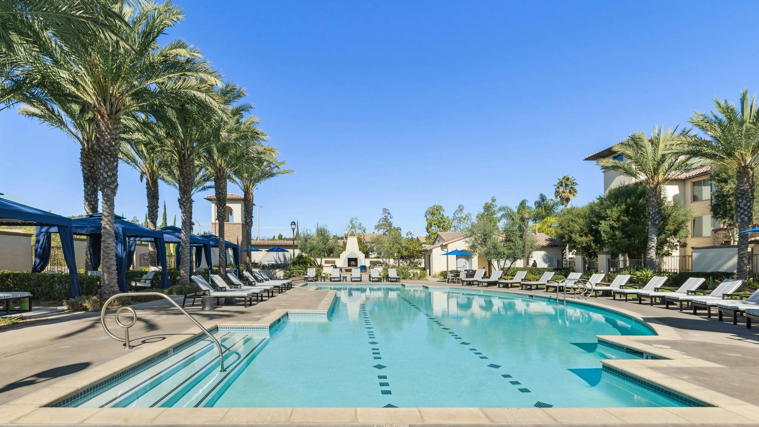 Daytime view of landscaped swimming pool with ample lounge seating and blue private cabanas at AMLI Spanish Hills apartments