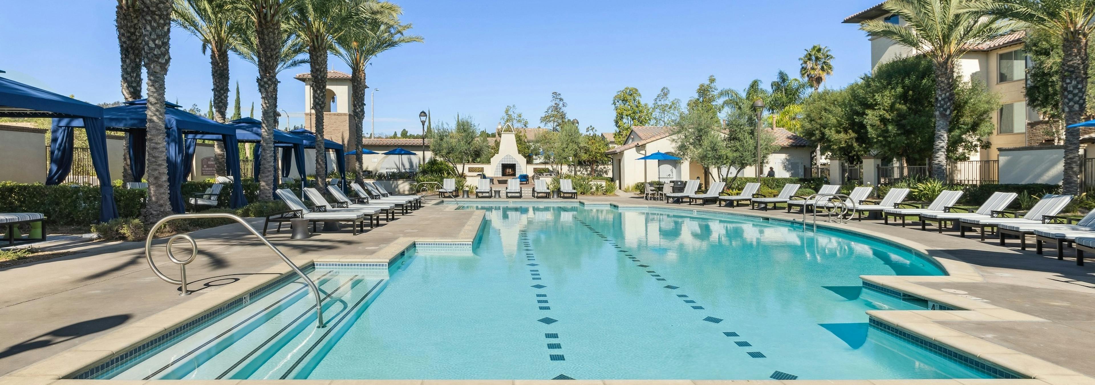 Daytime view of landscaped swimming pool with ample lounge seating and blue private cabanas at AMLI Spanish Hills apartments