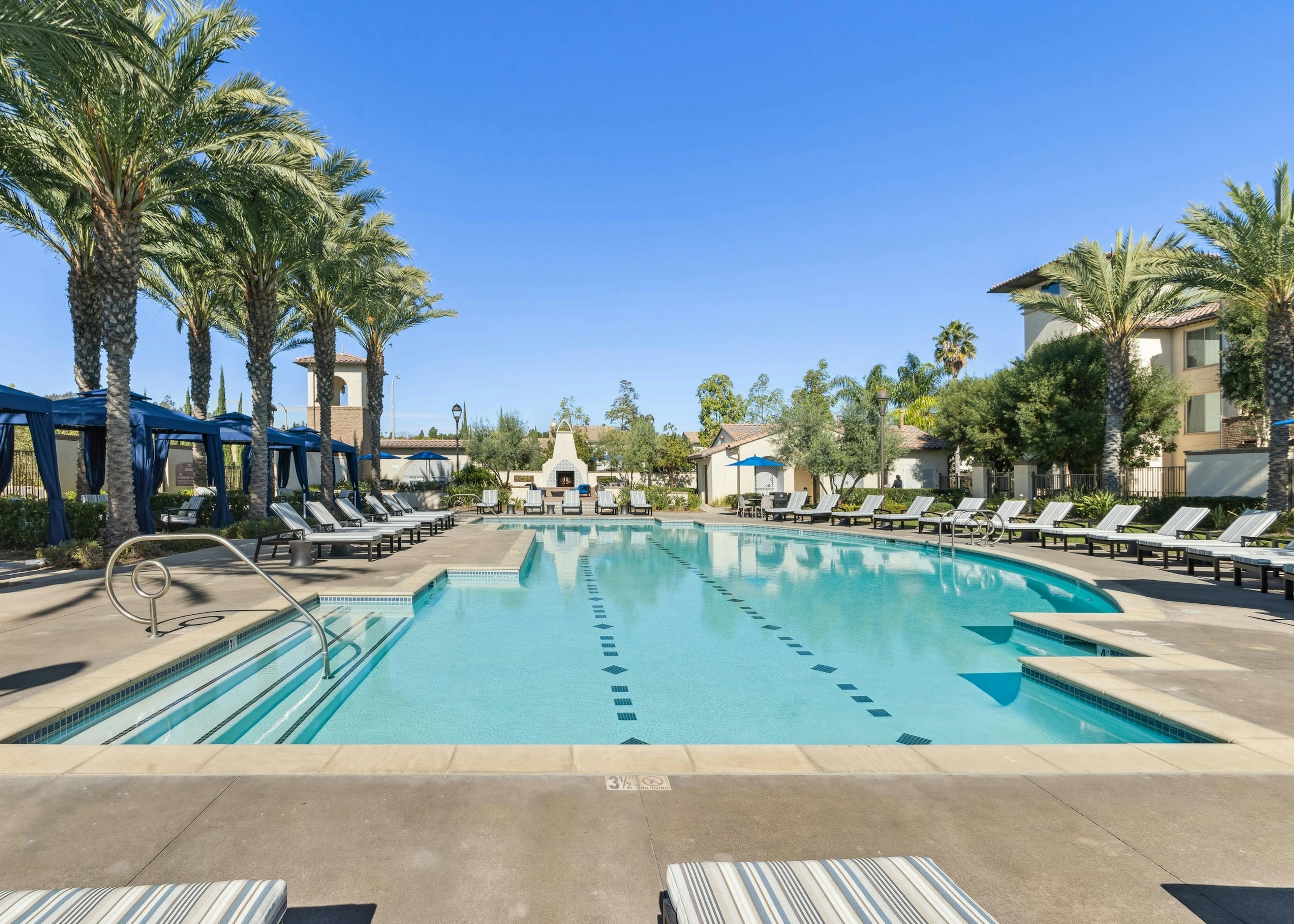 Daytime view of landscaped swimming pool with ample lounge seating and blue private cabanas at AMLI Spanish Hills apartments