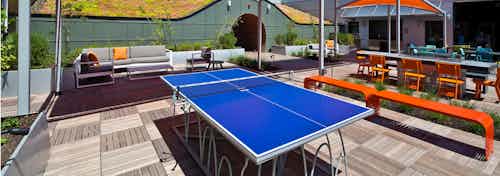 A beautiful sunny day of a blue ping pong table on AMLI South Lake Union rooftop deck with patio seating and fire pit