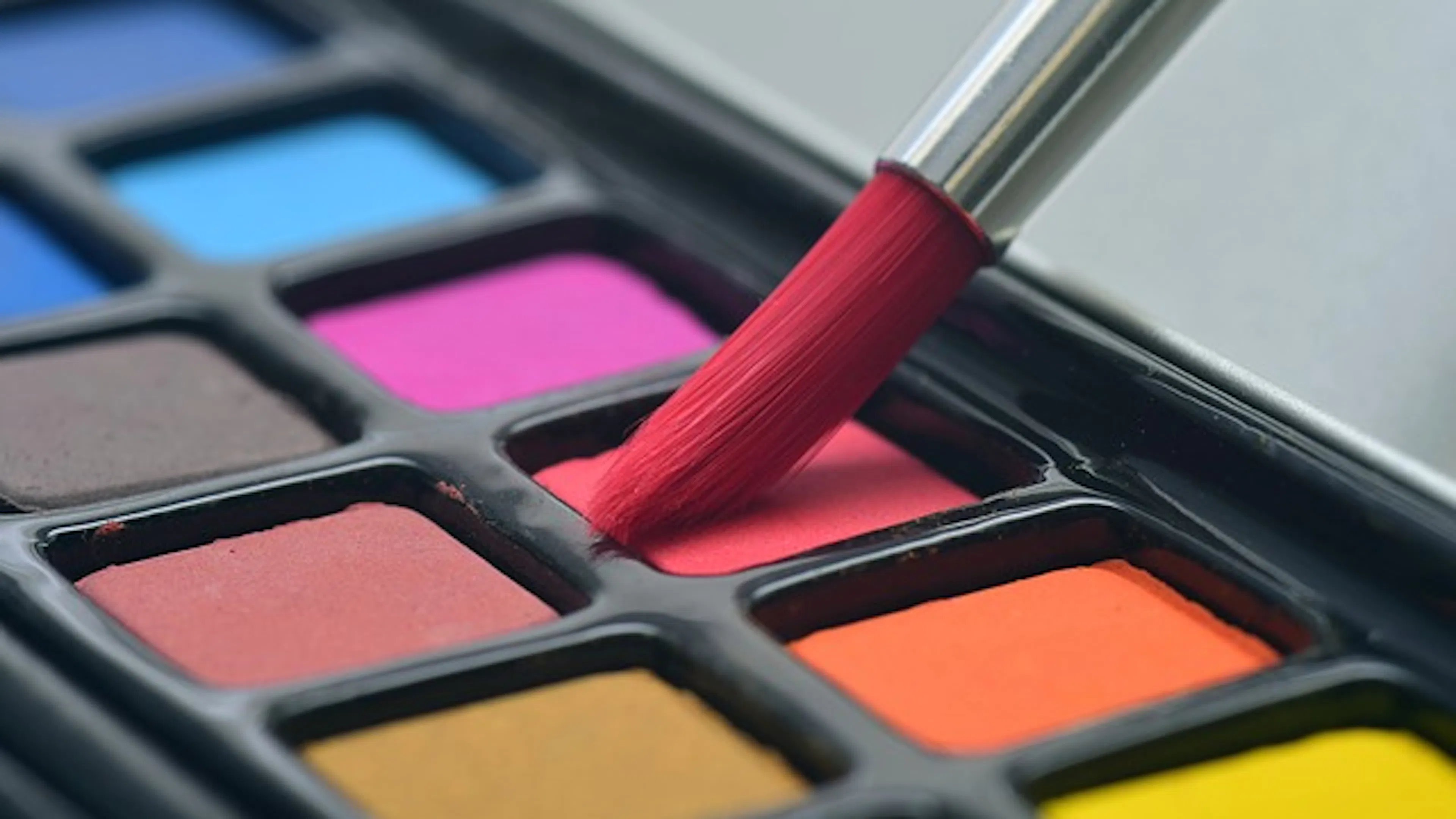 Close up of a round tip paintbrush dipping into a watercolor palate