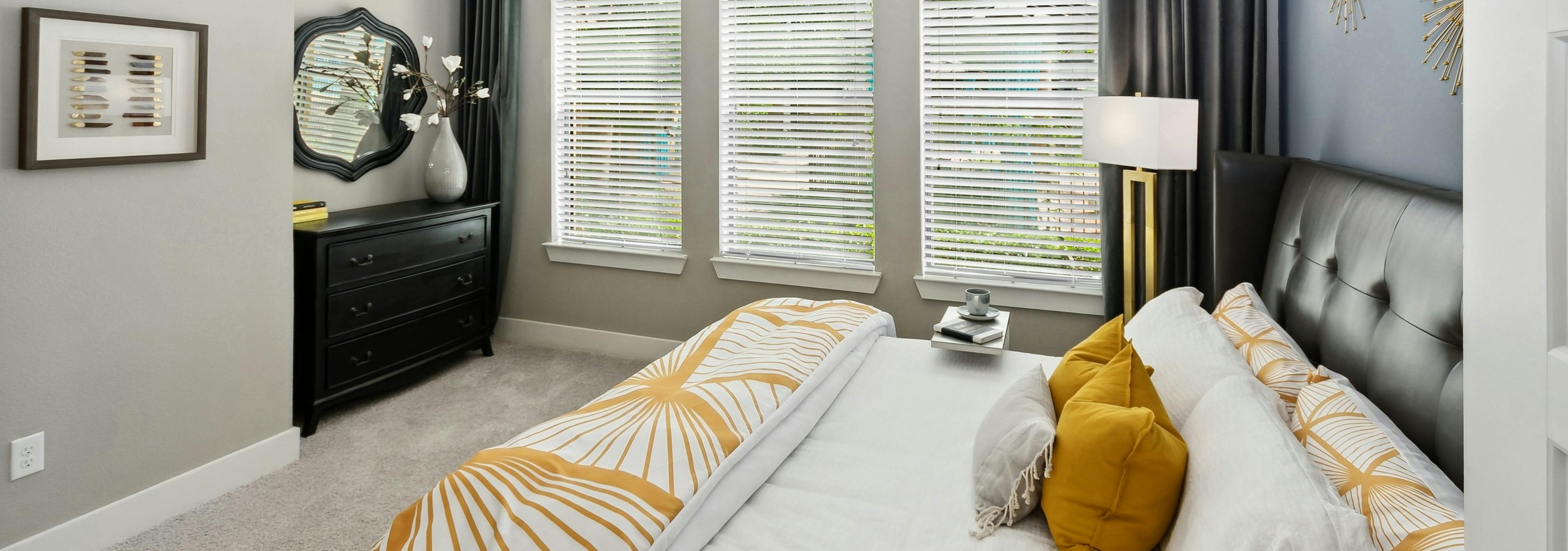 Interior view of AMLI Campion Trail bedroom with queen bed and 3 large windows with blinds next to black dresser