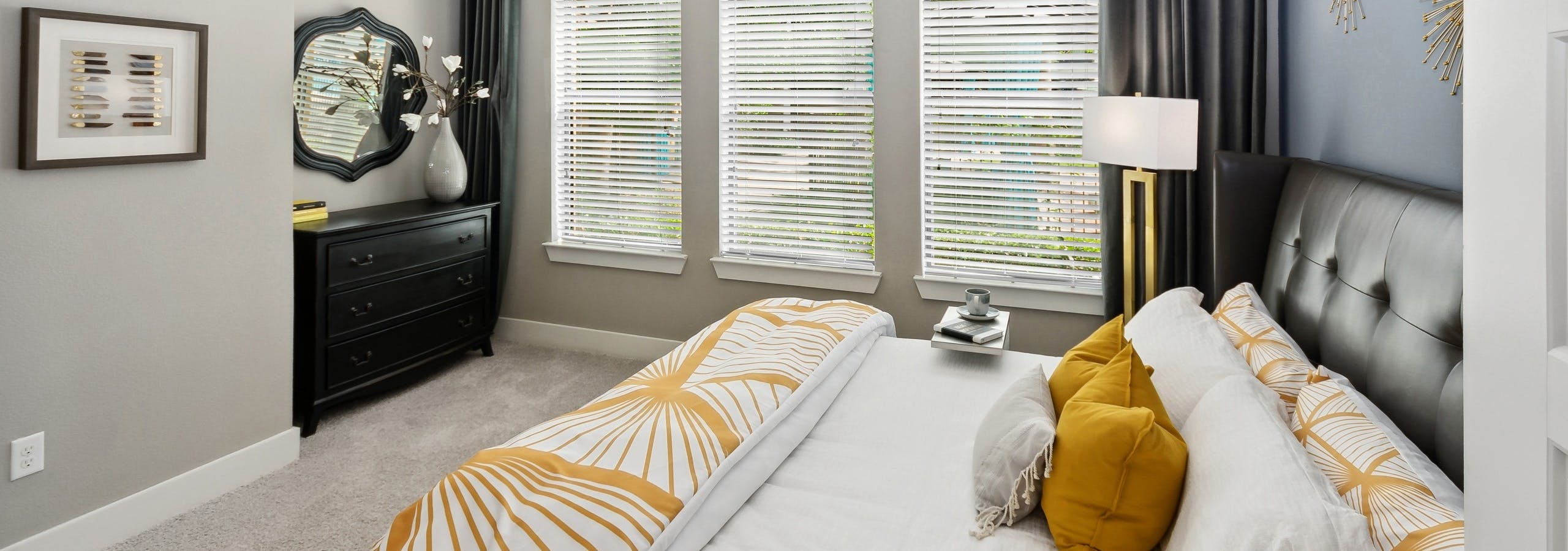 Interior view of AMLI Campion Trail bedroom with queen bed and 3 large windows with blinds next to black dresser