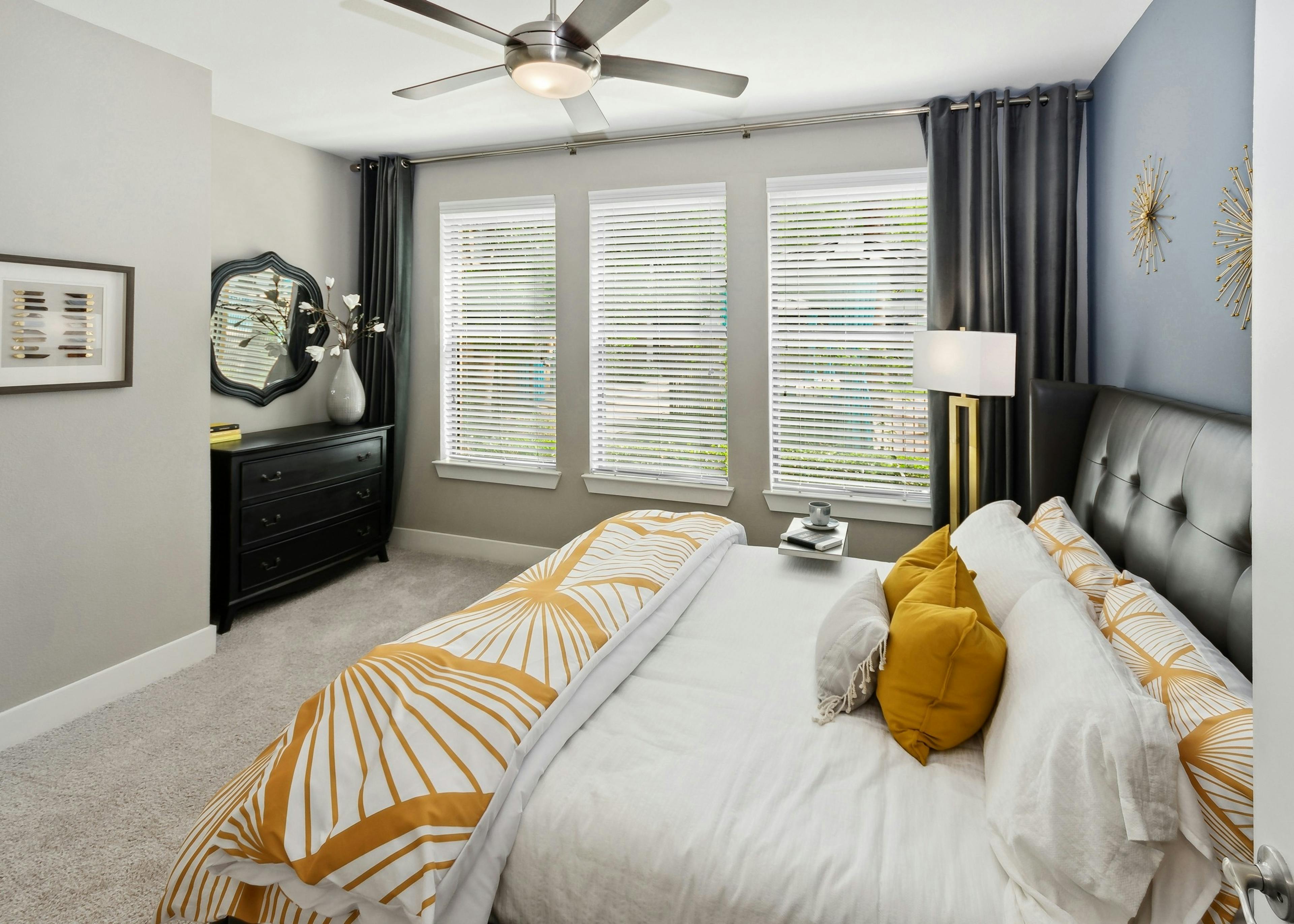 Interior view of AMLI Campion Trail bedroom with queen bed and 3 large windows with blinds next to black dresser