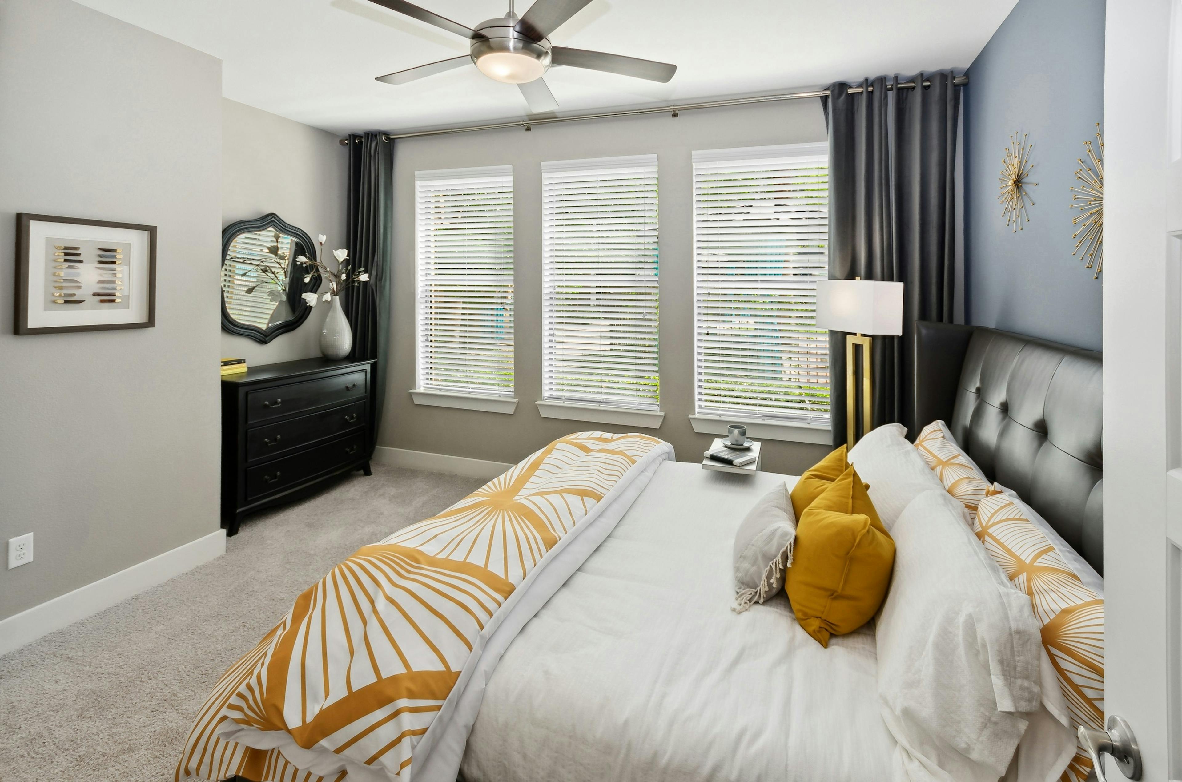 Interior view of AMLI Campion Trail bedroom with queen bed and 3 large windows with blinds next to black dresser