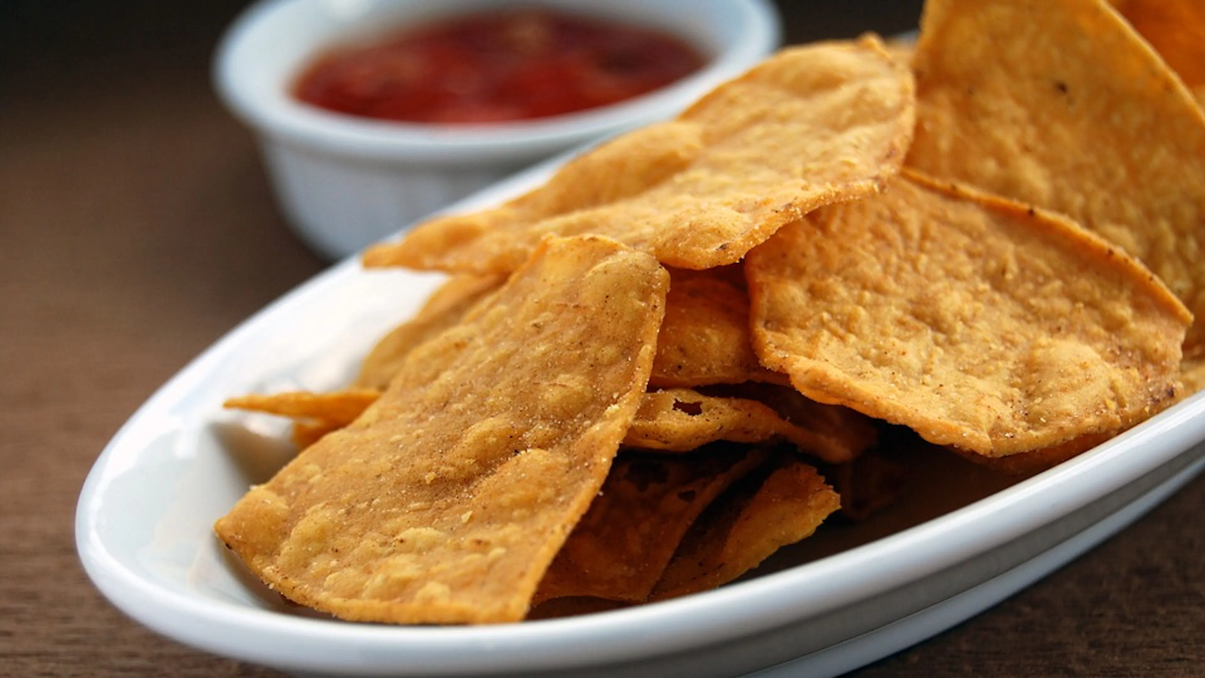 A plate of thick tortilla chips in front of a small white bowl full of salsa
