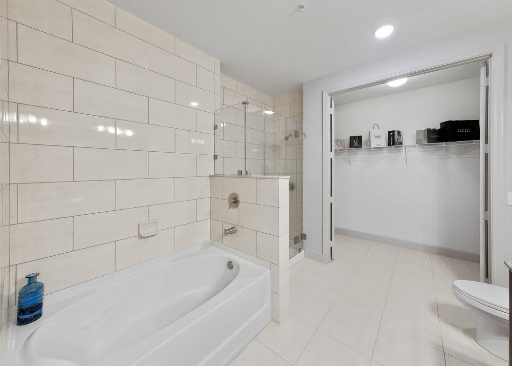 Interior view of AMLI 8800 apartment bathroom with double vanity, mirror, toilet, glass shower enclosure and walk-in closet