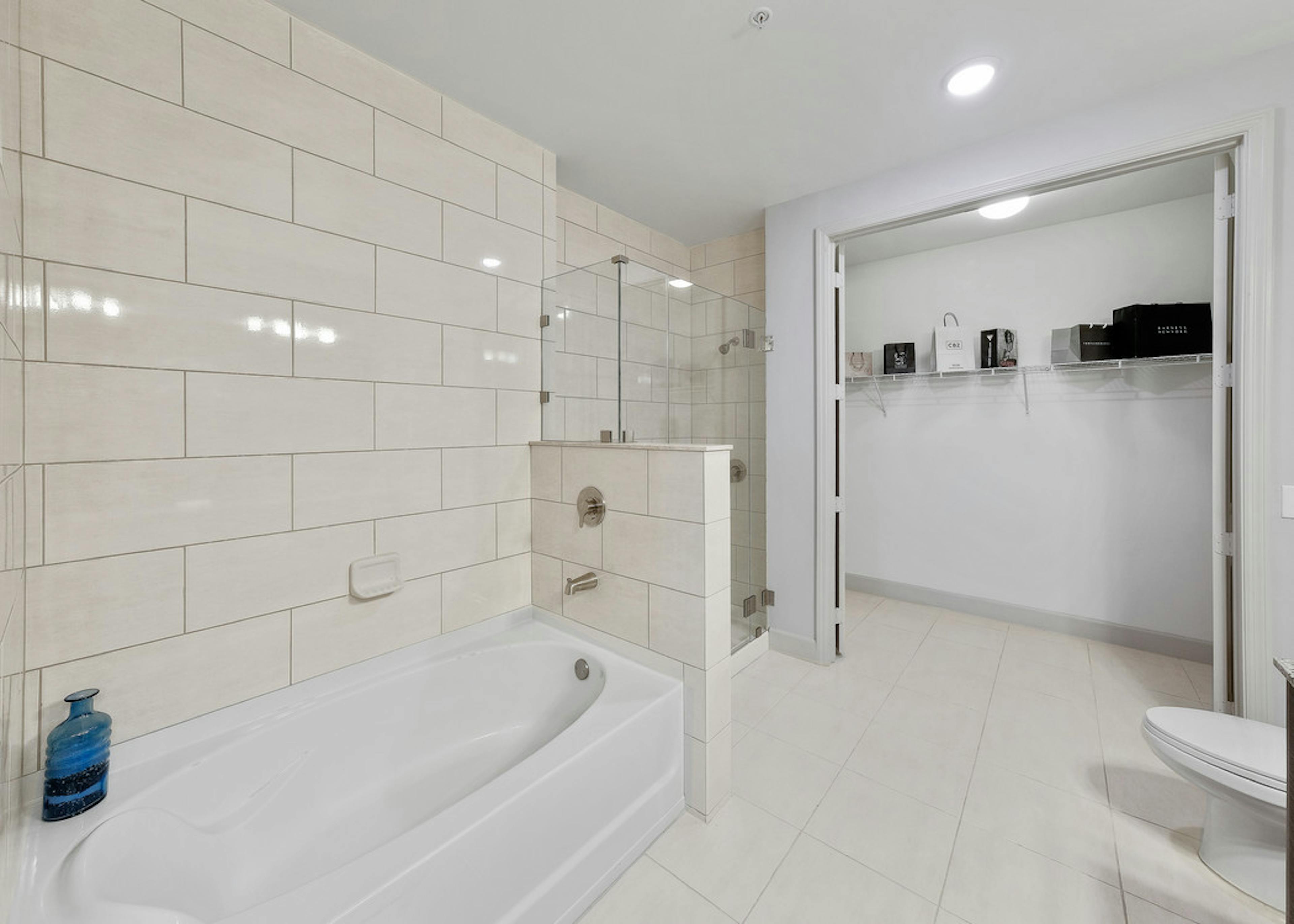 Interior view of AMLI 8800 apartment bathroom with double vanity, mirror, toilet, glass shower enclosure and walk-in closet