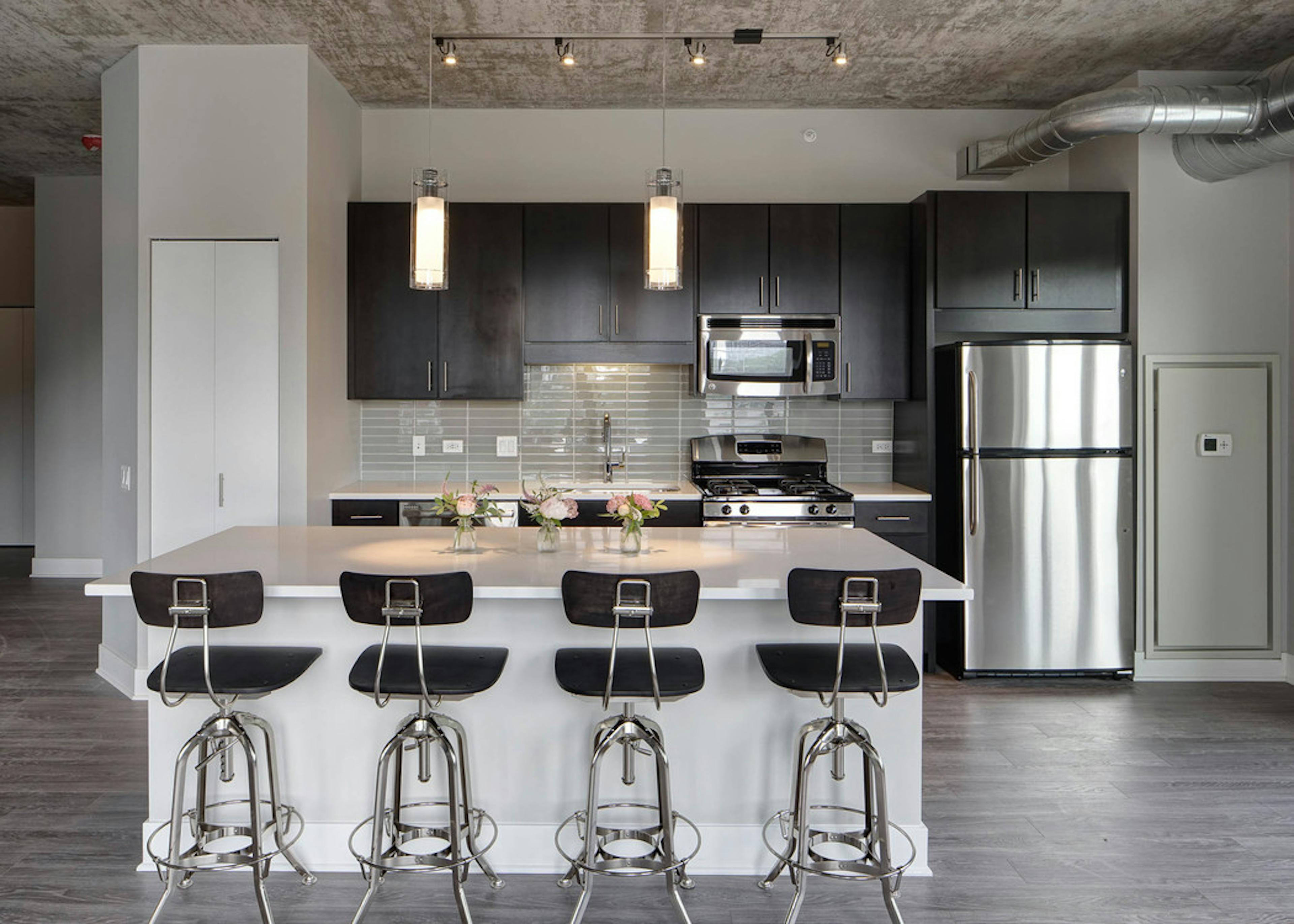 Interior view of an AMLI Lofts kitchen with dark wooden cabinets and a quartz island with four black bar stools