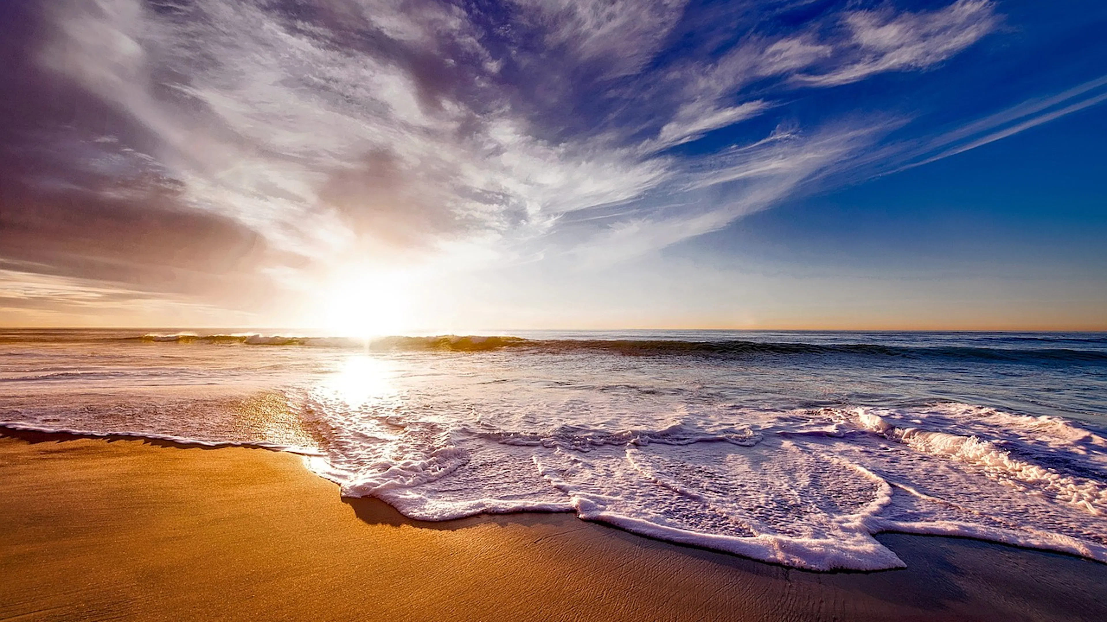 A stunning sunset over a gentle beach and frothing wave breaks