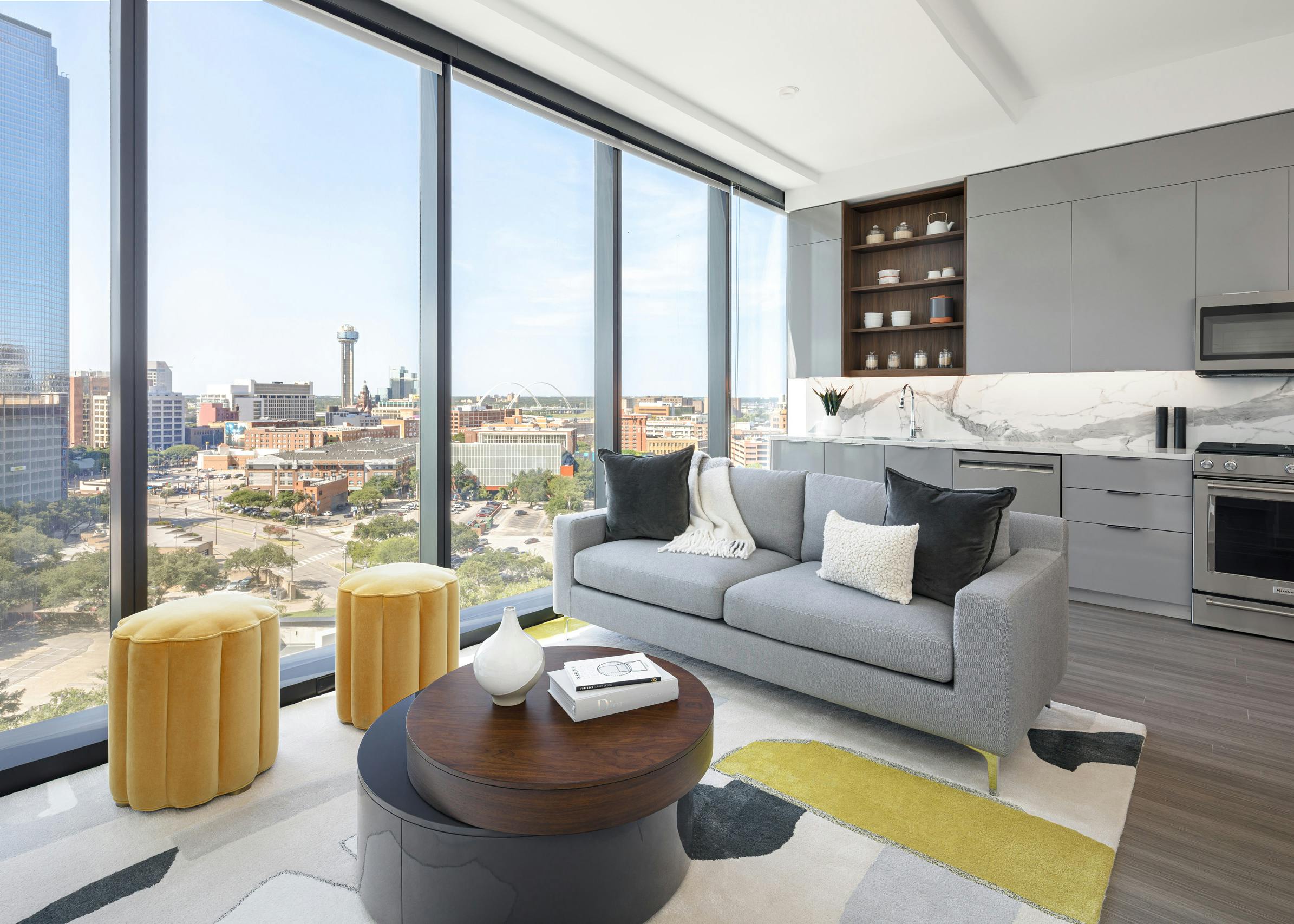 AMLI Fountain Place living room with gray couch and coffee table next to large wall of windows and light gray kitchen behind