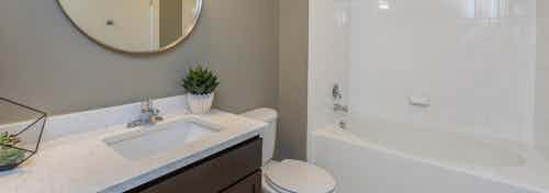 AMLI 5350 bathroom with a dark wood vanity sink with white countertops and a round mirror with tan walls and white shower tub