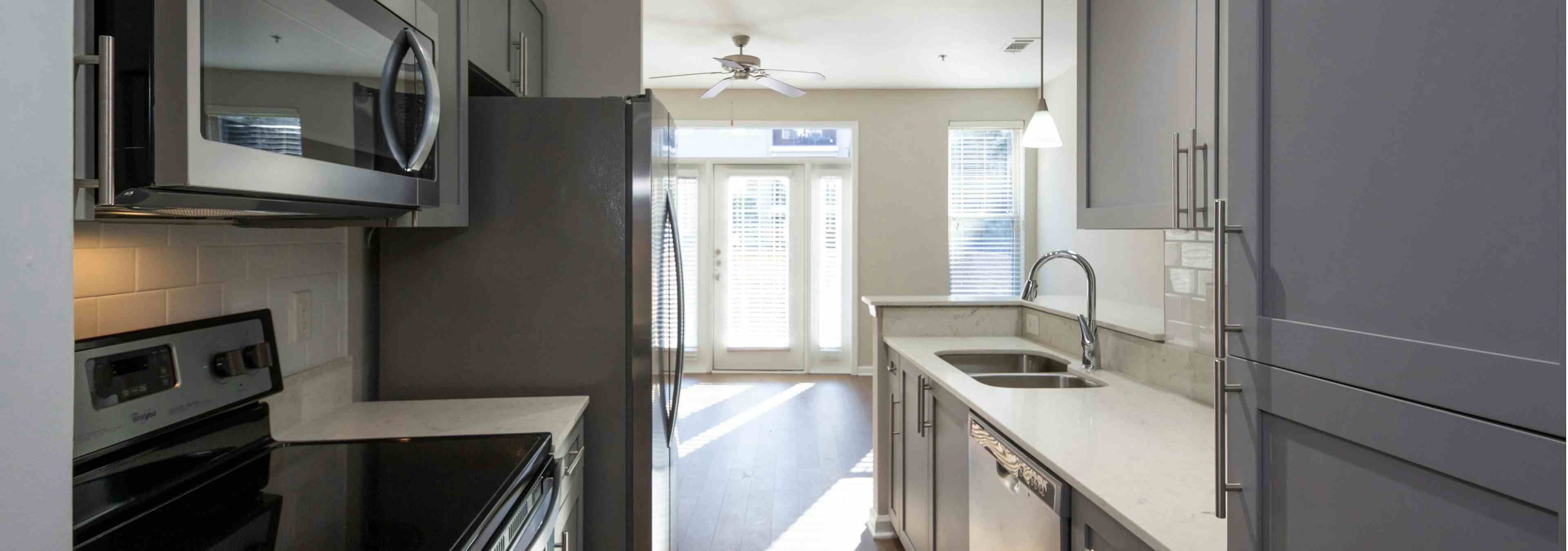 Interior view of AMLI Lindbergh apartment kitchen with grey cabinets and white countertops with stainless steel appliances