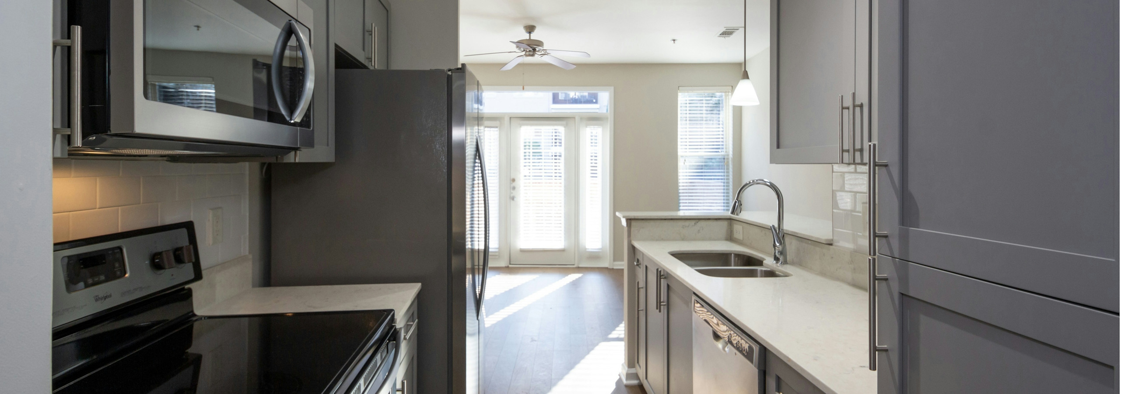 Interior view of AMLI Lindbergh apartment kitchen with grey cabinets and white countertops with stainless steel appliances