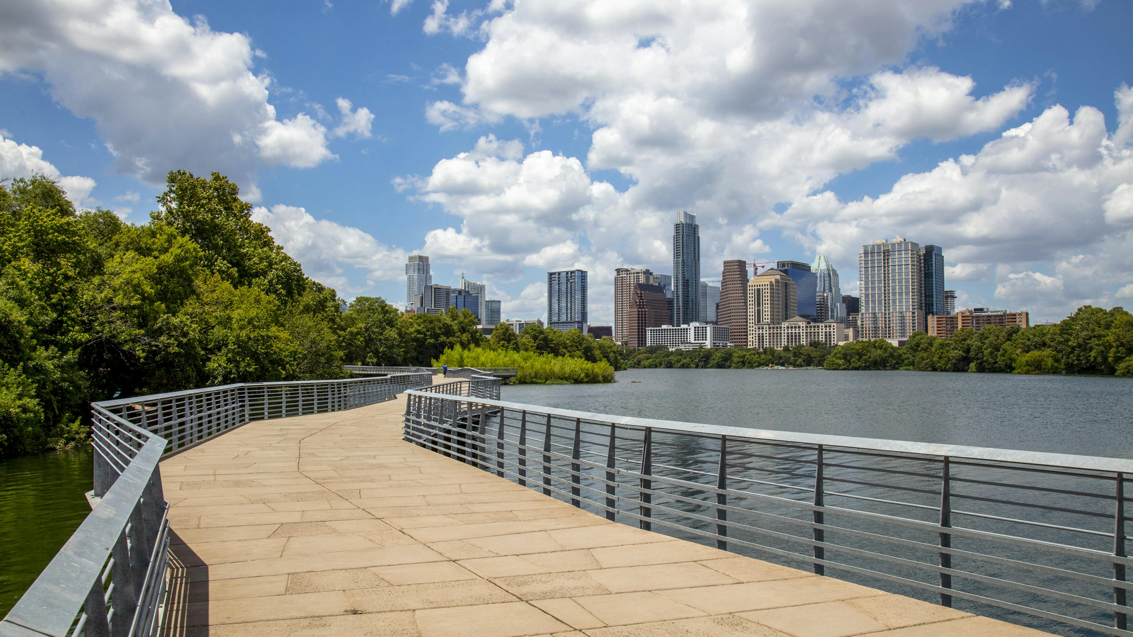 Lakefront boardwalk with metal railings by AMLI South Shore apartments with views of downtown Austin skyline and lush greenery