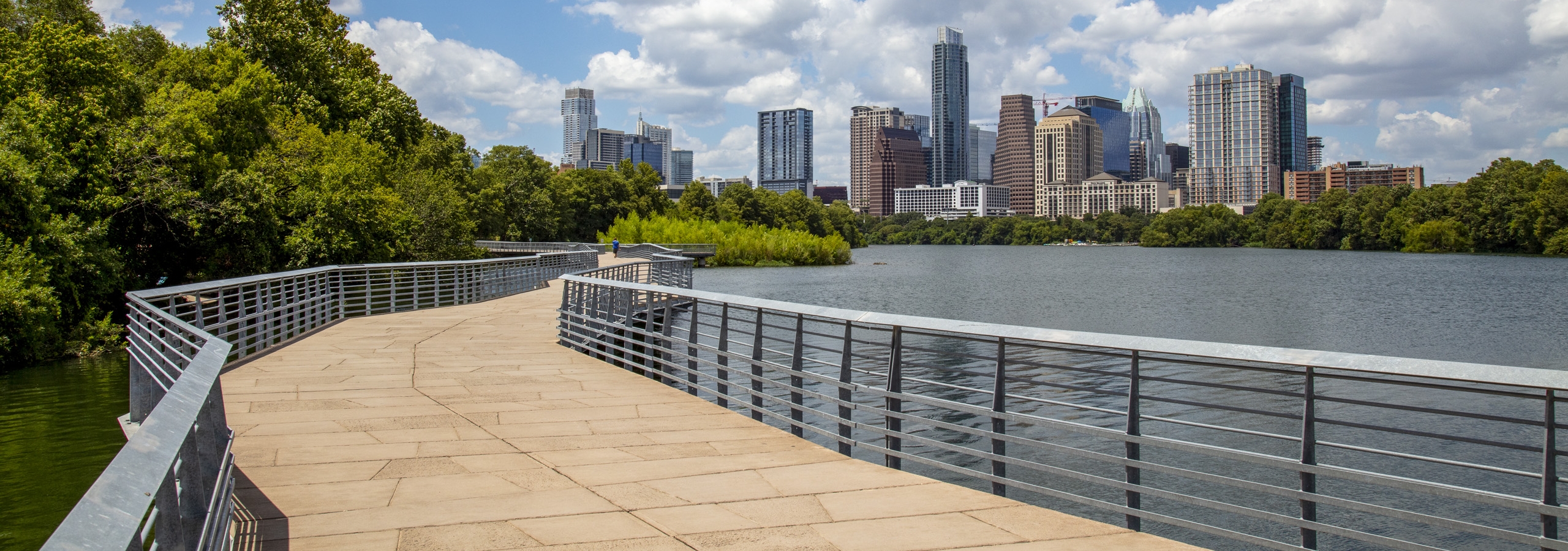 Lakefront boardwalk with metal railings by AMLI South Shore apartments with views of downtown Austin skyline and lush greenery