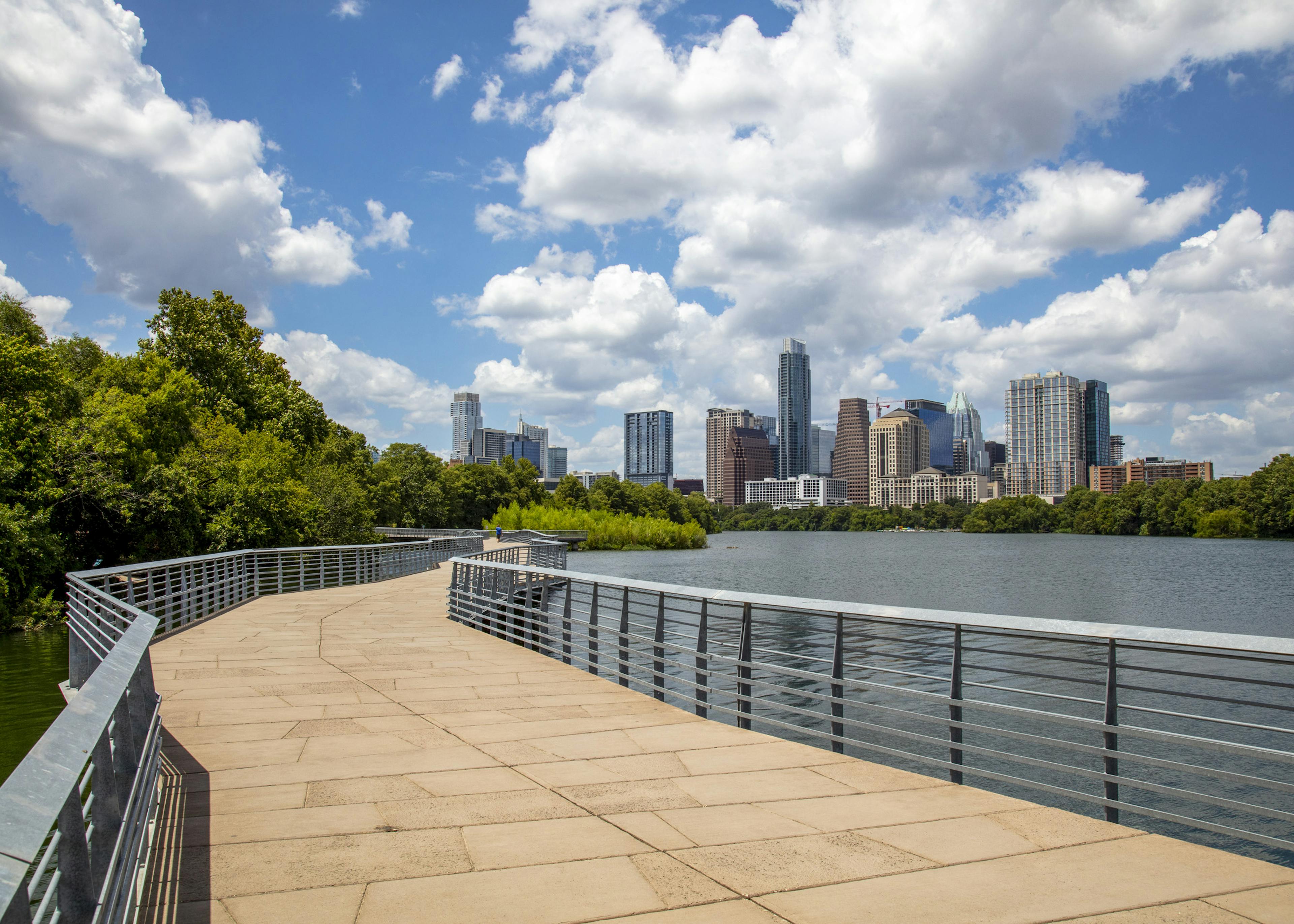 Lakefront boardwalk with metal railings by AMLI South Shore apartments with views of downtown Austin skyline and lush greenery
