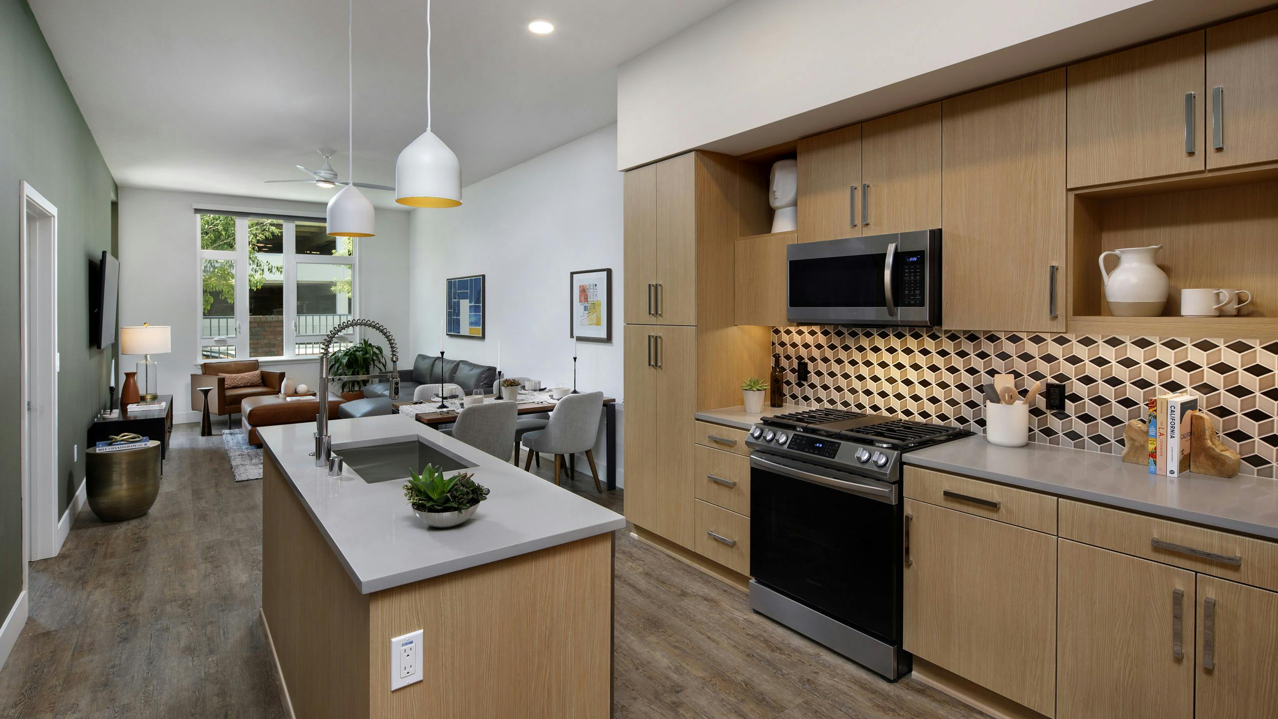 Interior of AMLI Old Pasadena apartment kitchen with light cabinets, and checkered backsplash facing spacious living room