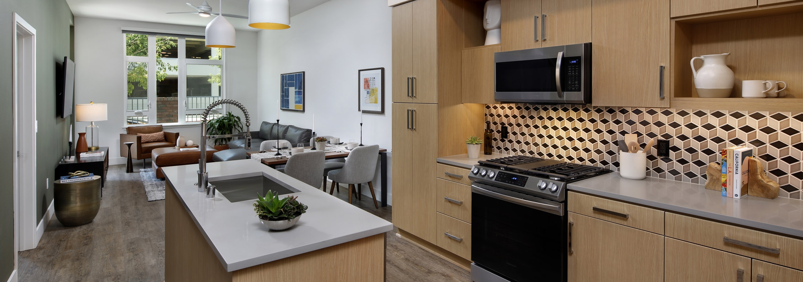 Interior of AMLI Old Pasadena apartment kitchen with light cabinets, and checkered backsplash facing spacious living room