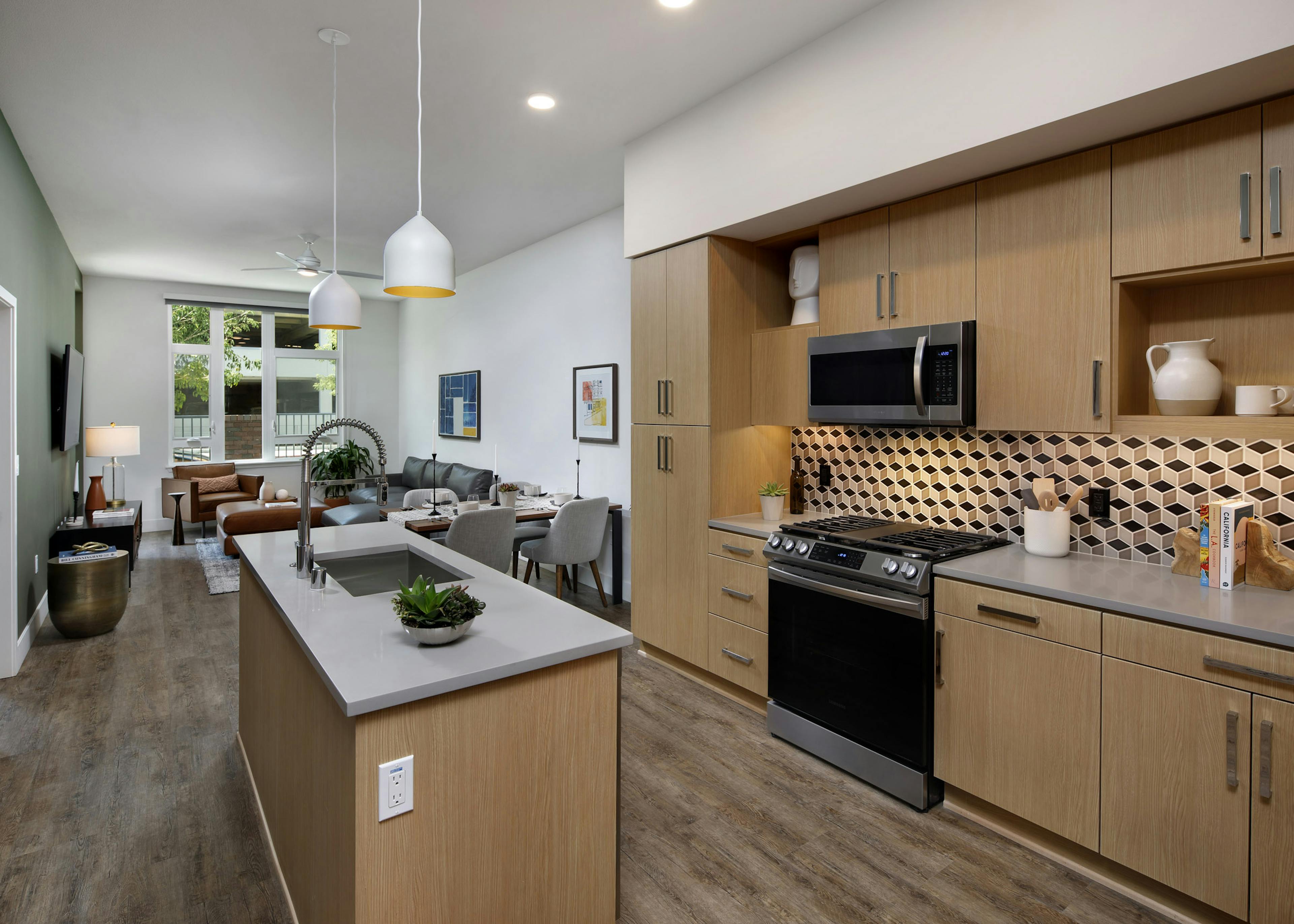 Interior of AMLI Old Pasadena apartment kitchen with light cabinets, and checkered backsplash facing spacious living room
