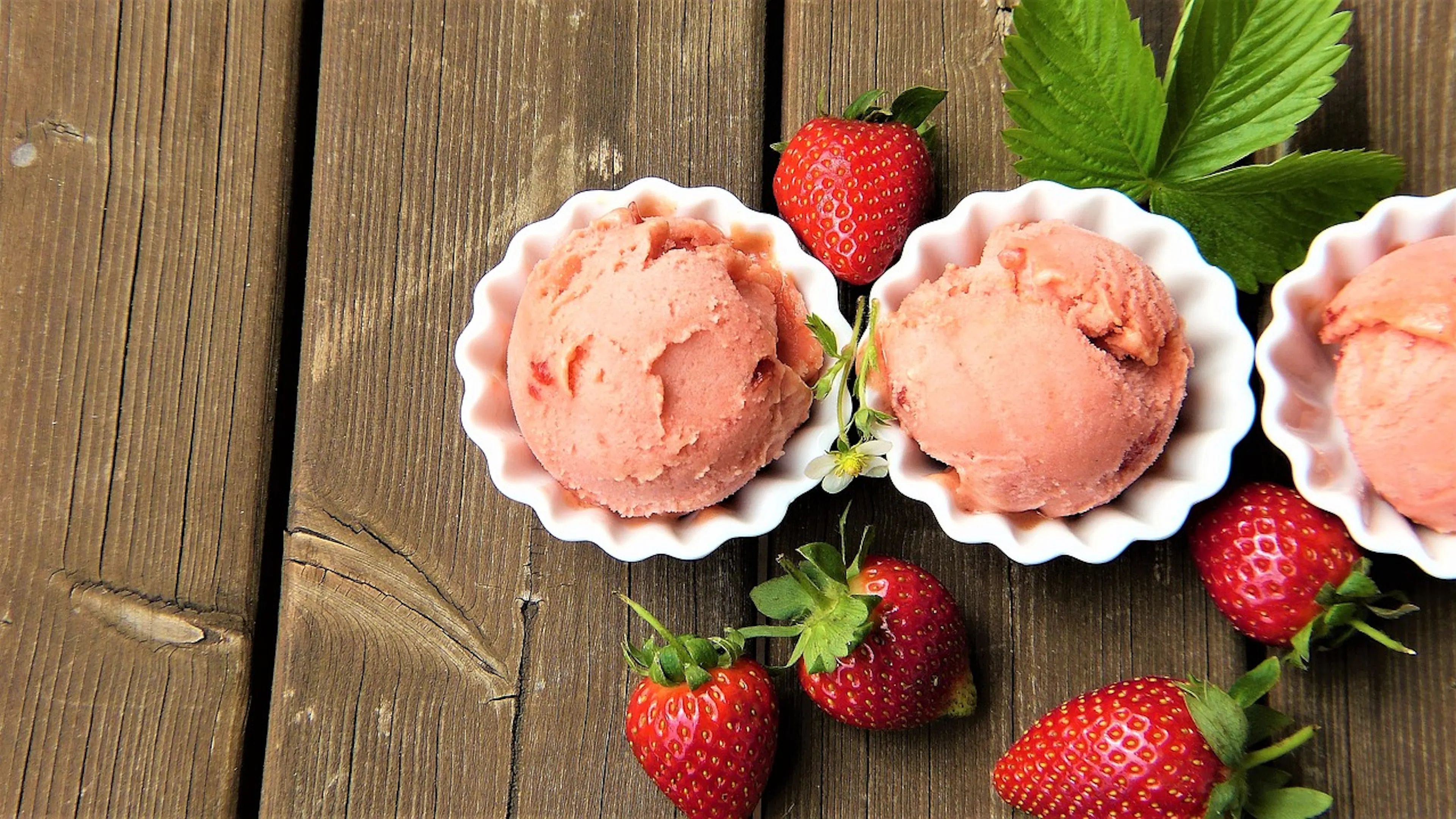 Three white dessert bowls with strawberry ice cream in each