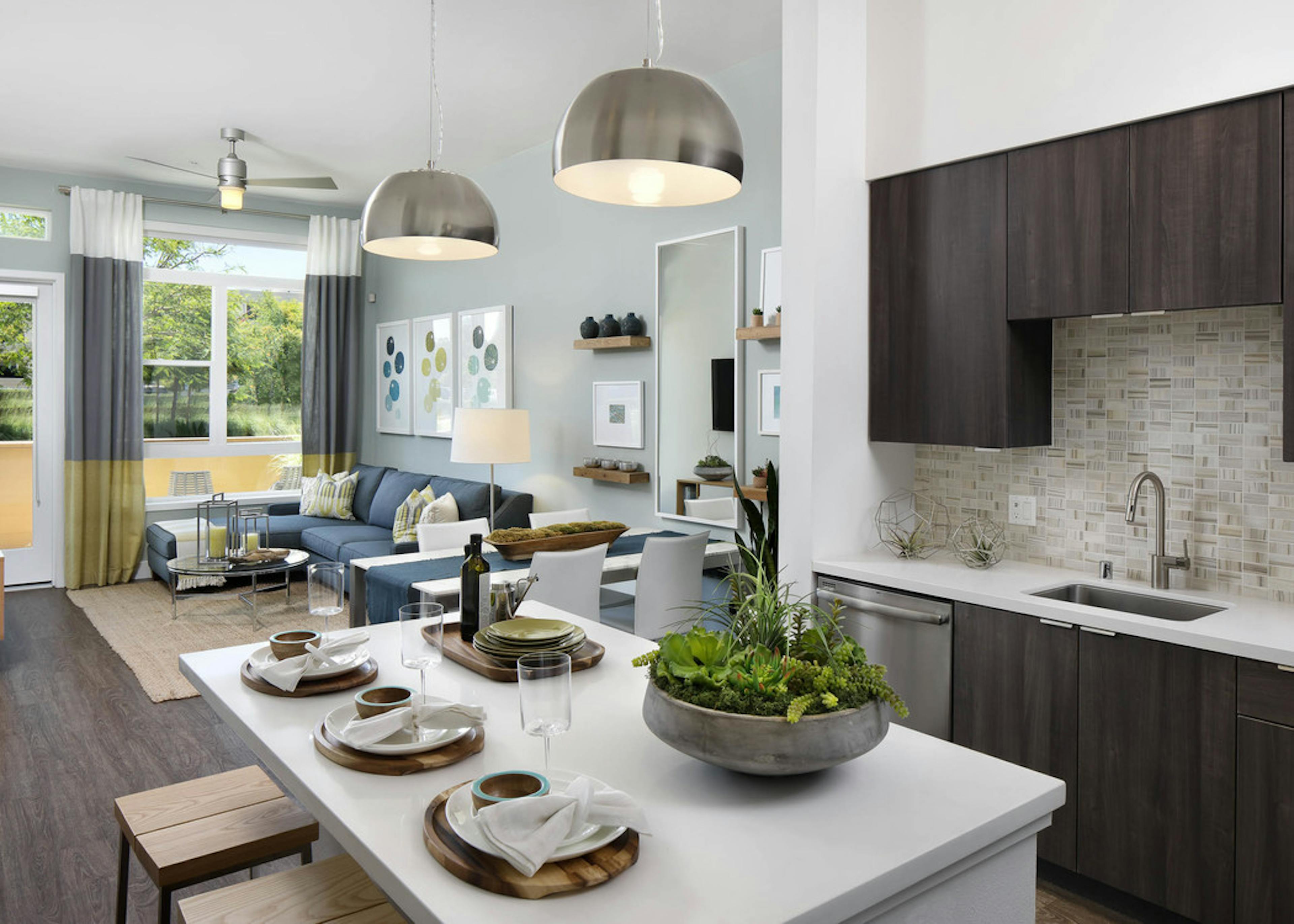 Interior of AMLI Uptown Orange apartment kitchen with dark wood cabinets and furnished living room with hard wood floors