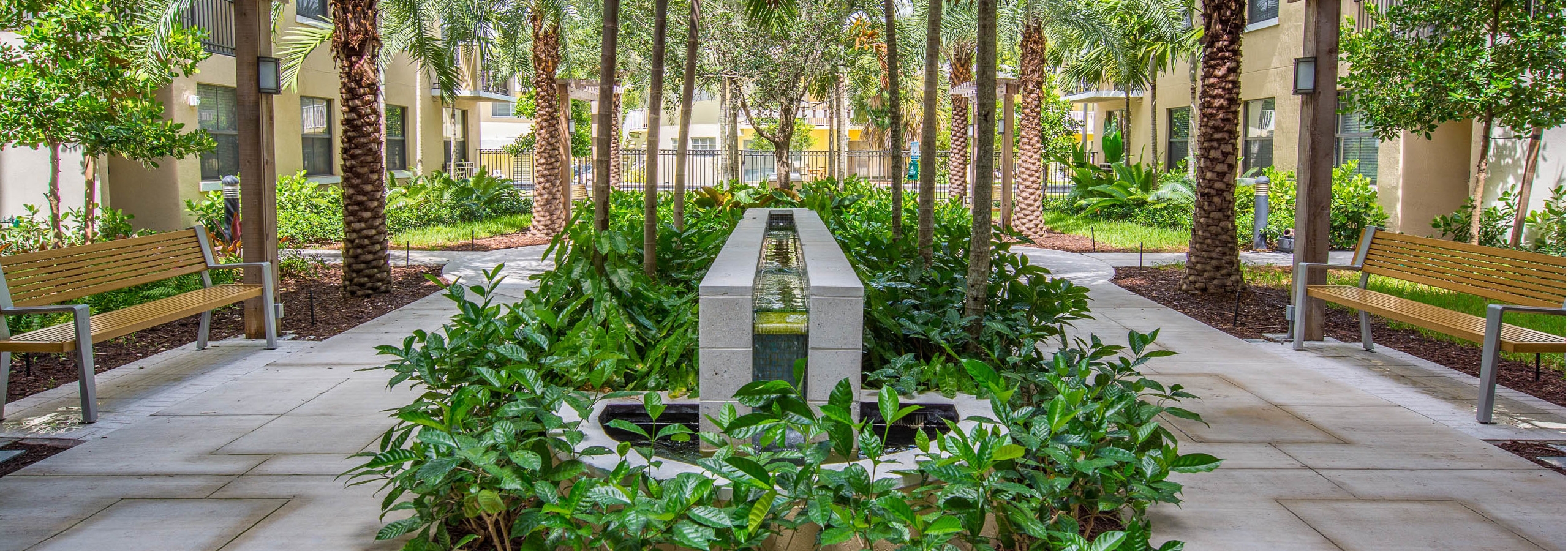 Exterior view of lush landscaped courtyard at AMLI Dadeland with park benches and a tranquil fountain in the center