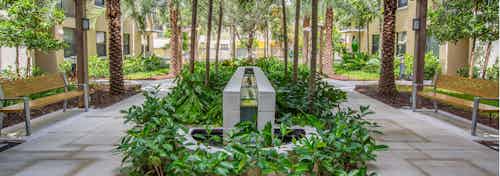 Exterior view of lush landscaped courtyard at AMLI Dadeland with park benches and a tranquil fountain in the center