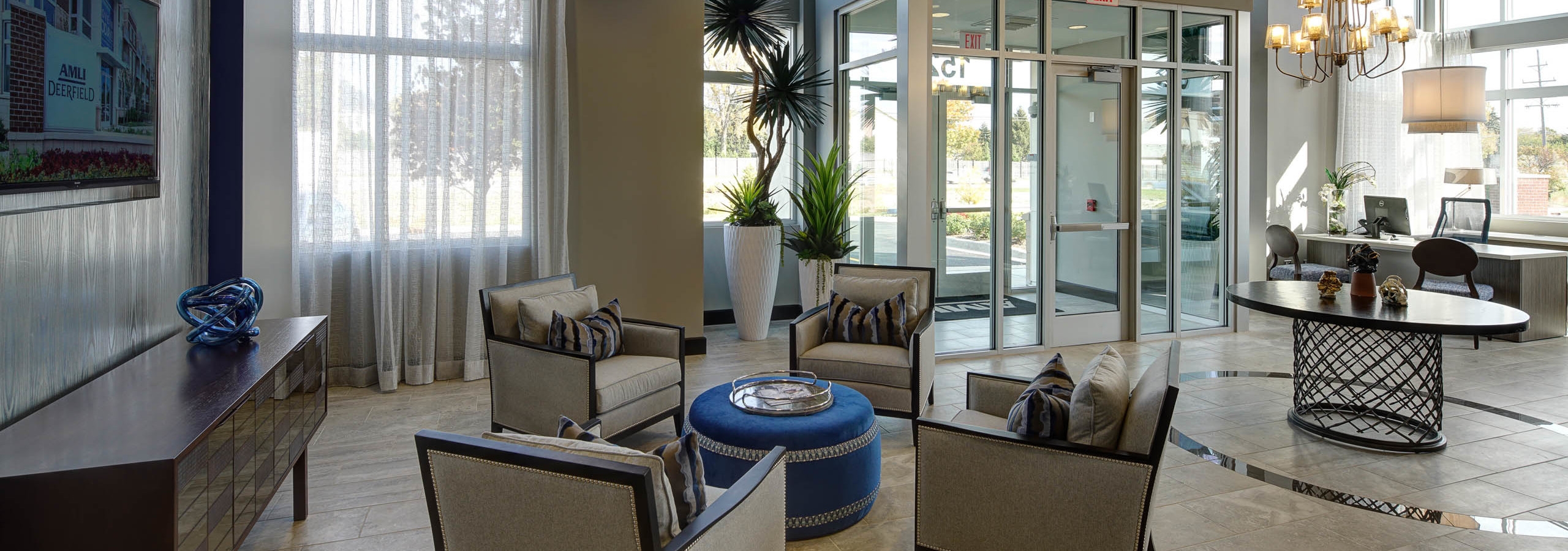 Bright interior of AMLI Deerfield office with sitting area with TV on side wall and leasing desk in the background