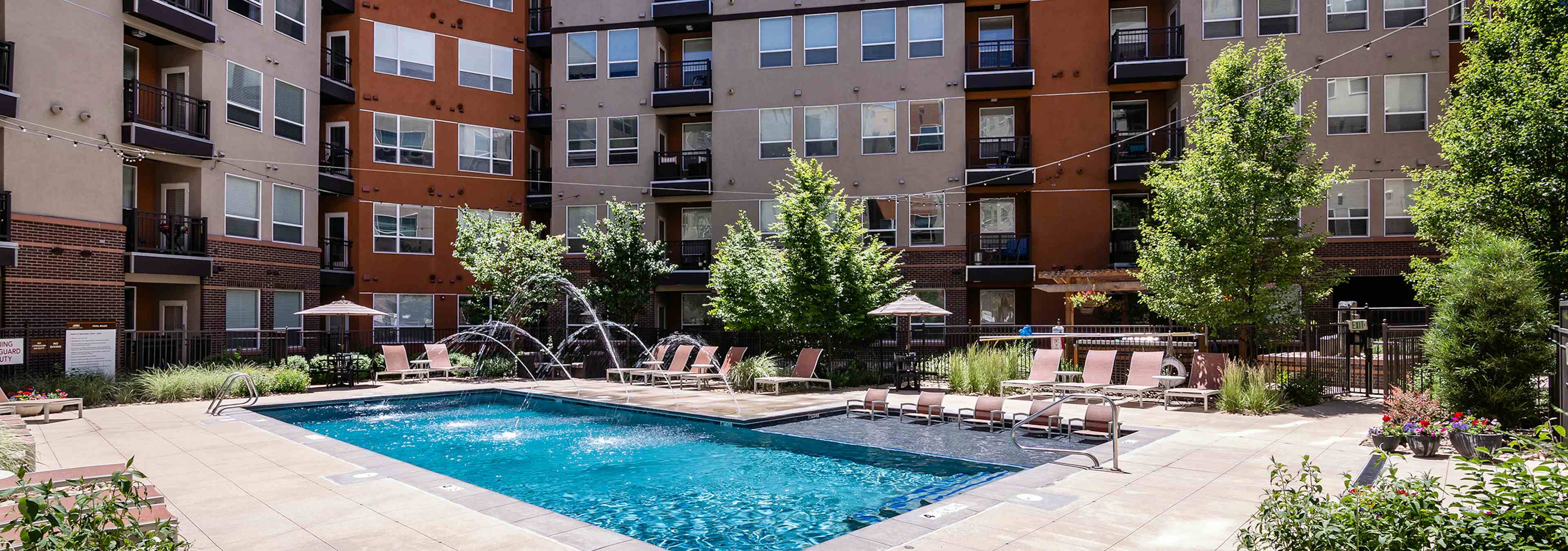 A pool at AMLI Riverfront Park apartments with water fountain streams coming out of the pool and lounge chairs and umbrellas