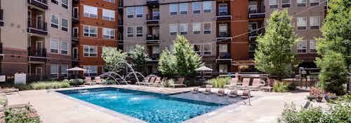 A pool at AMLI Riverfront Park apartments with water fountain streams coming out of the pool and lounge chairs and umbrellas