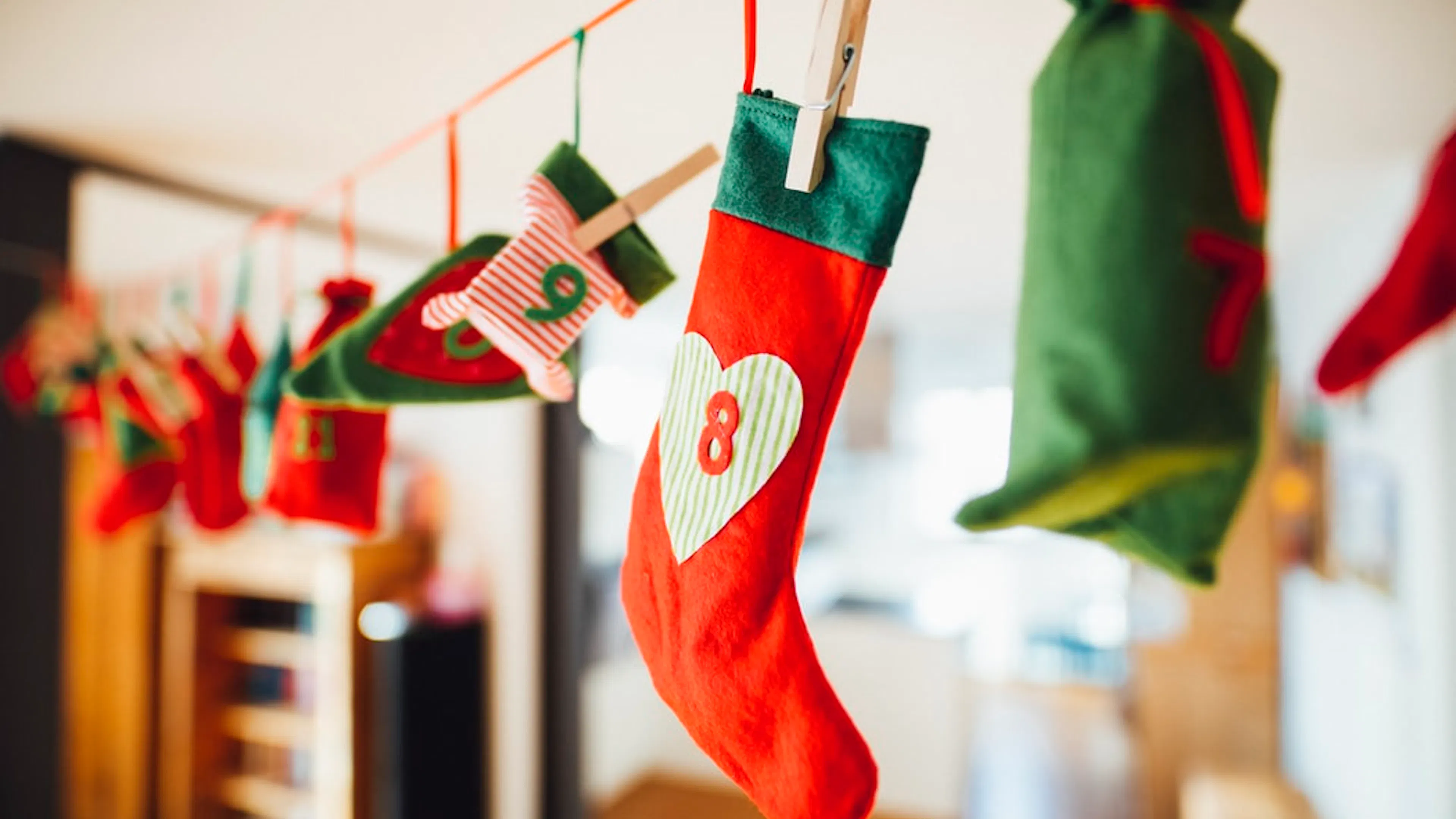 A string holding 25 small advent Christmas stockings with numbers 1 to 25 on them and all decorated with red green and white colors