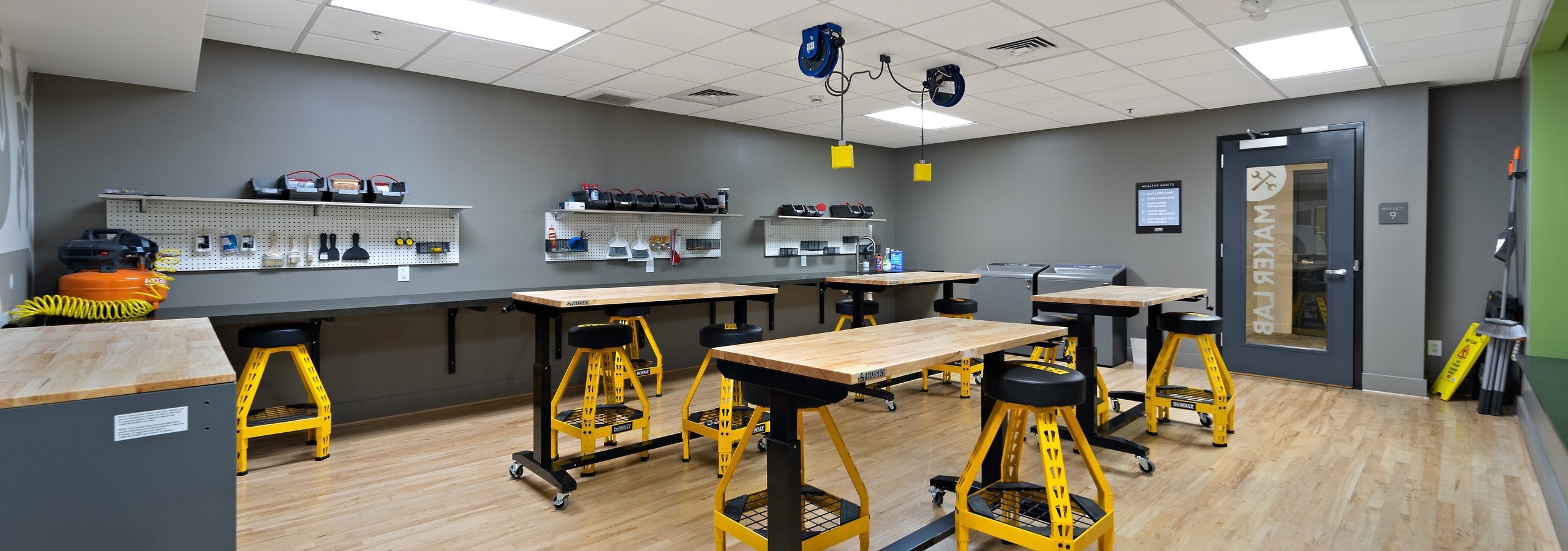 Maker lab at AMLI Bellevue Park apartments with wood worktables with yellow and black stools and wall of tools on gray wall