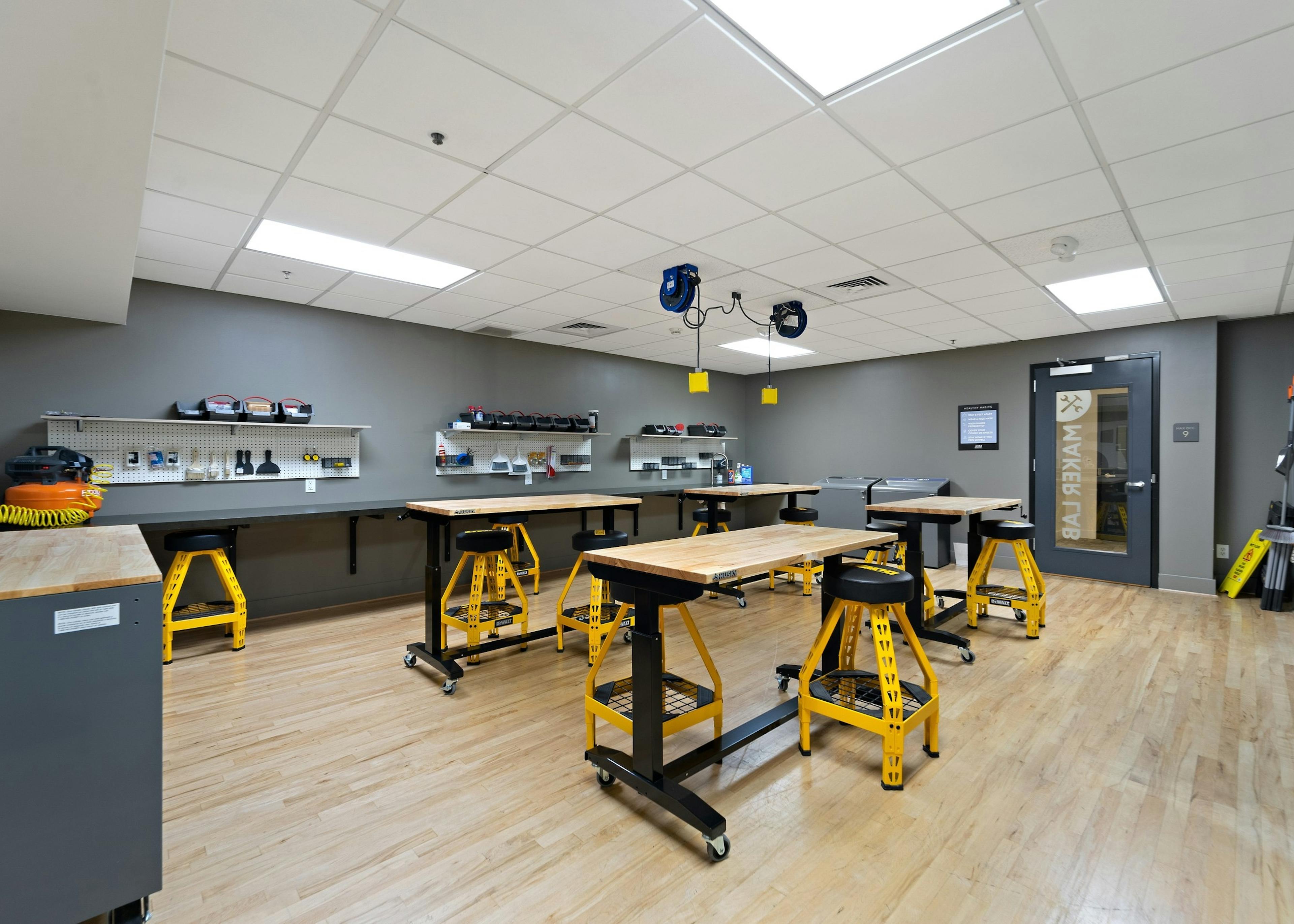 
Maker lab at AMLI Bellevue Park apartments with wood worktables with yellow and black stools and wall of tools on gray wall