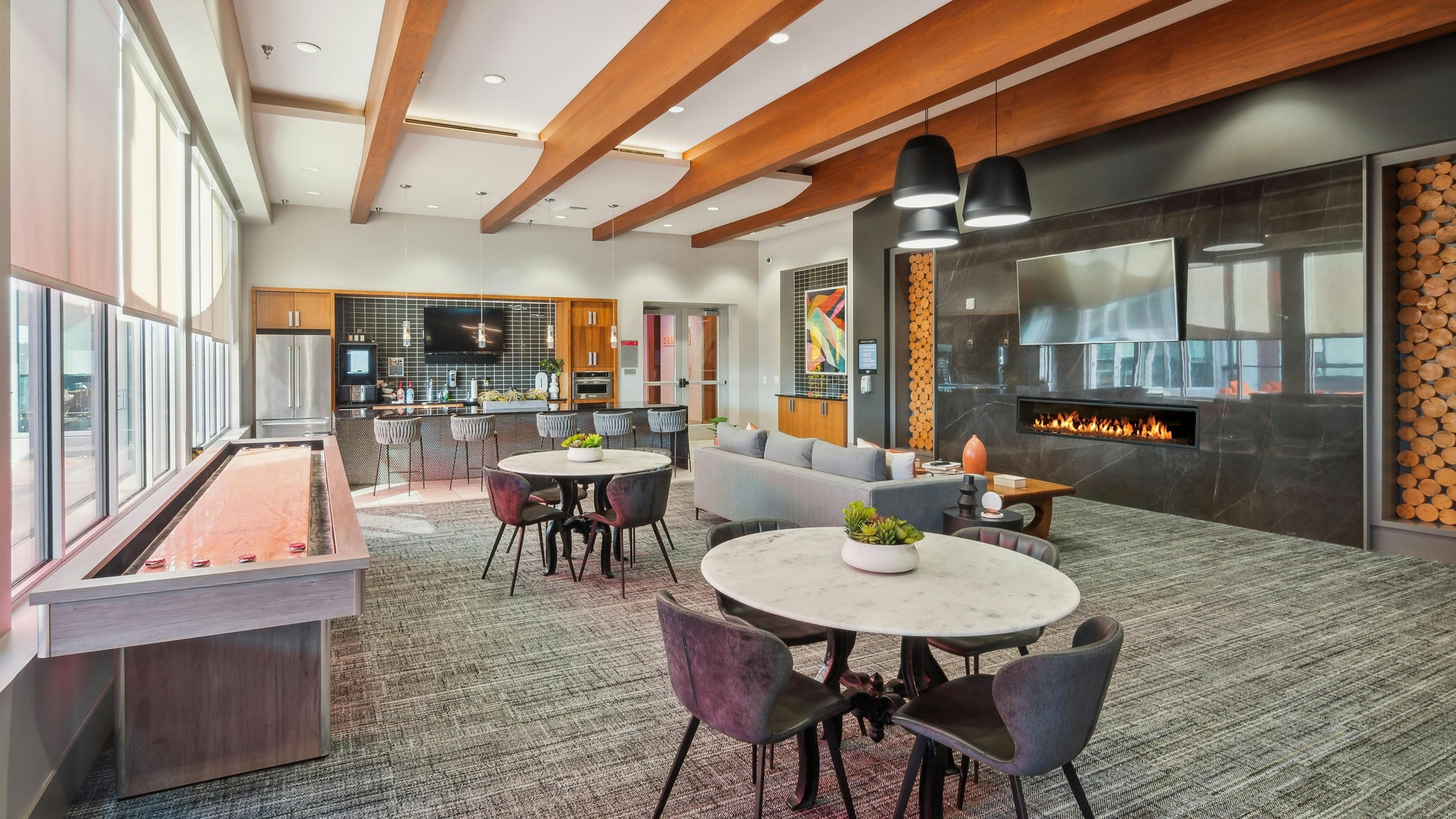 Clubroom at AMLI Denargo Market with wood rafters and game table and tables and chairs and couch across from fireplace and TV 