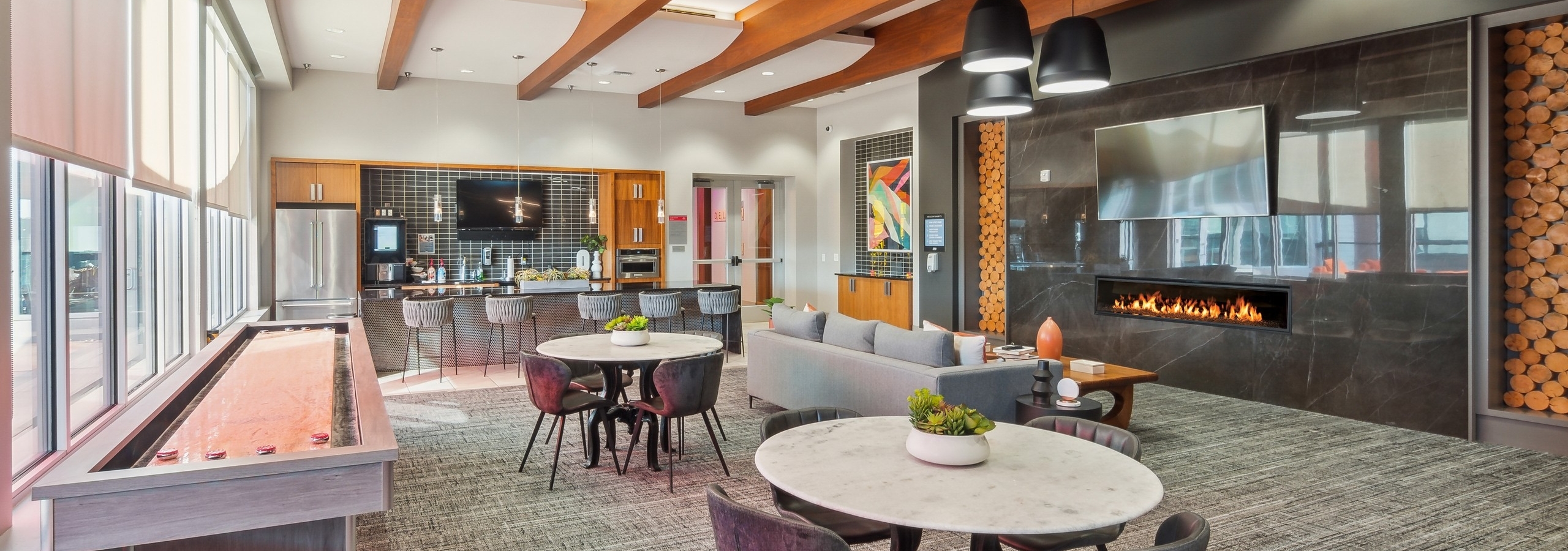 Clubroom at AMLI Denargo Market with wood rafters and game table and tables and chairs and couch across from fireplace and TV
