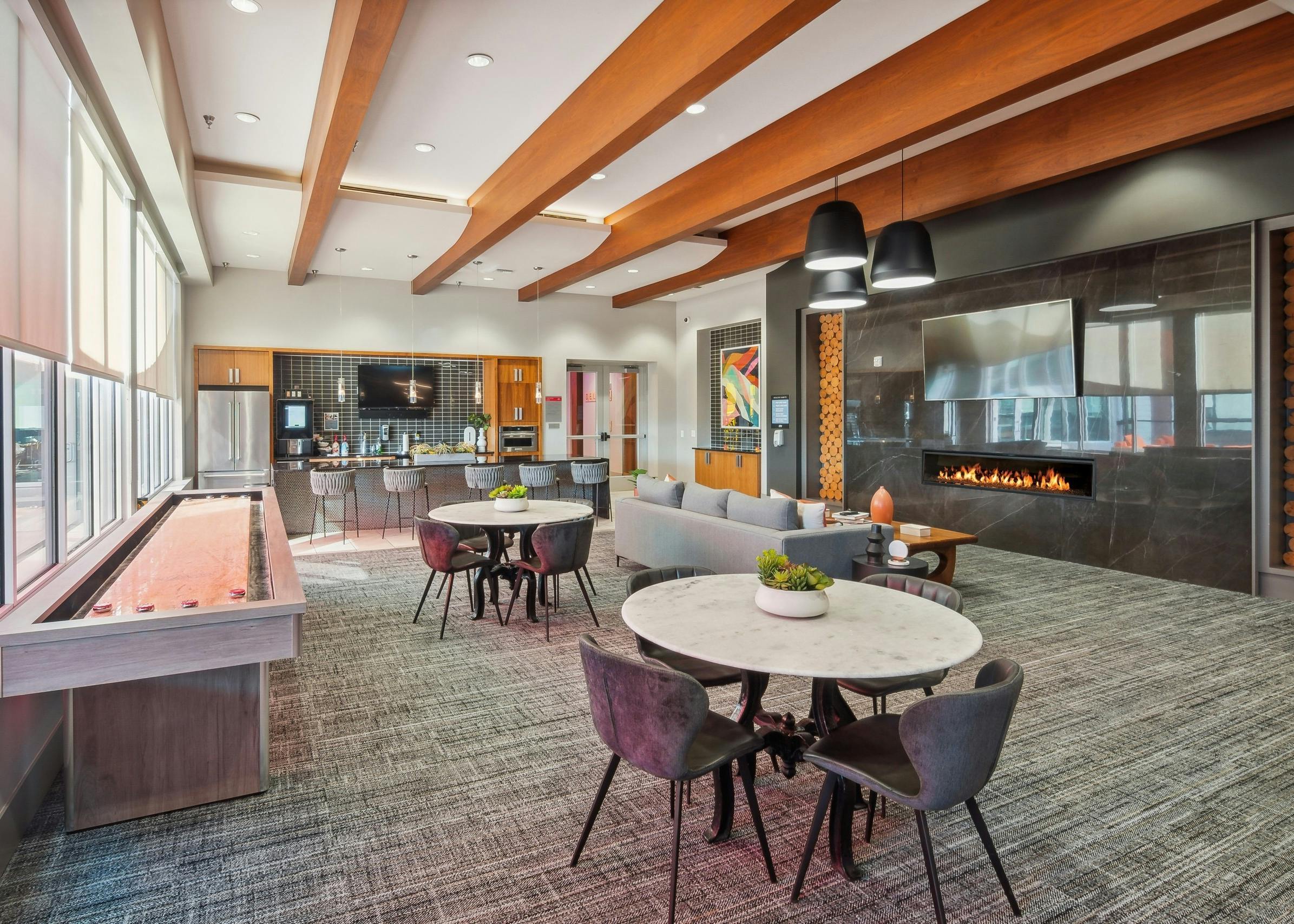 Clubroom at AMLI Denargo Market with wood rafters and game table and tables and chairs and couch across from fireplace and TV