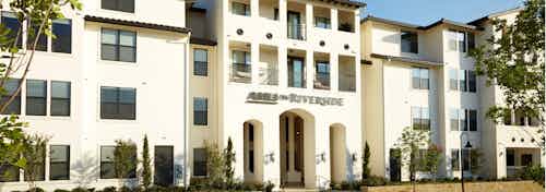 Exterior of AMLI on Riverside white stucco building facade with small trees lining the entry way and larger trees nearby