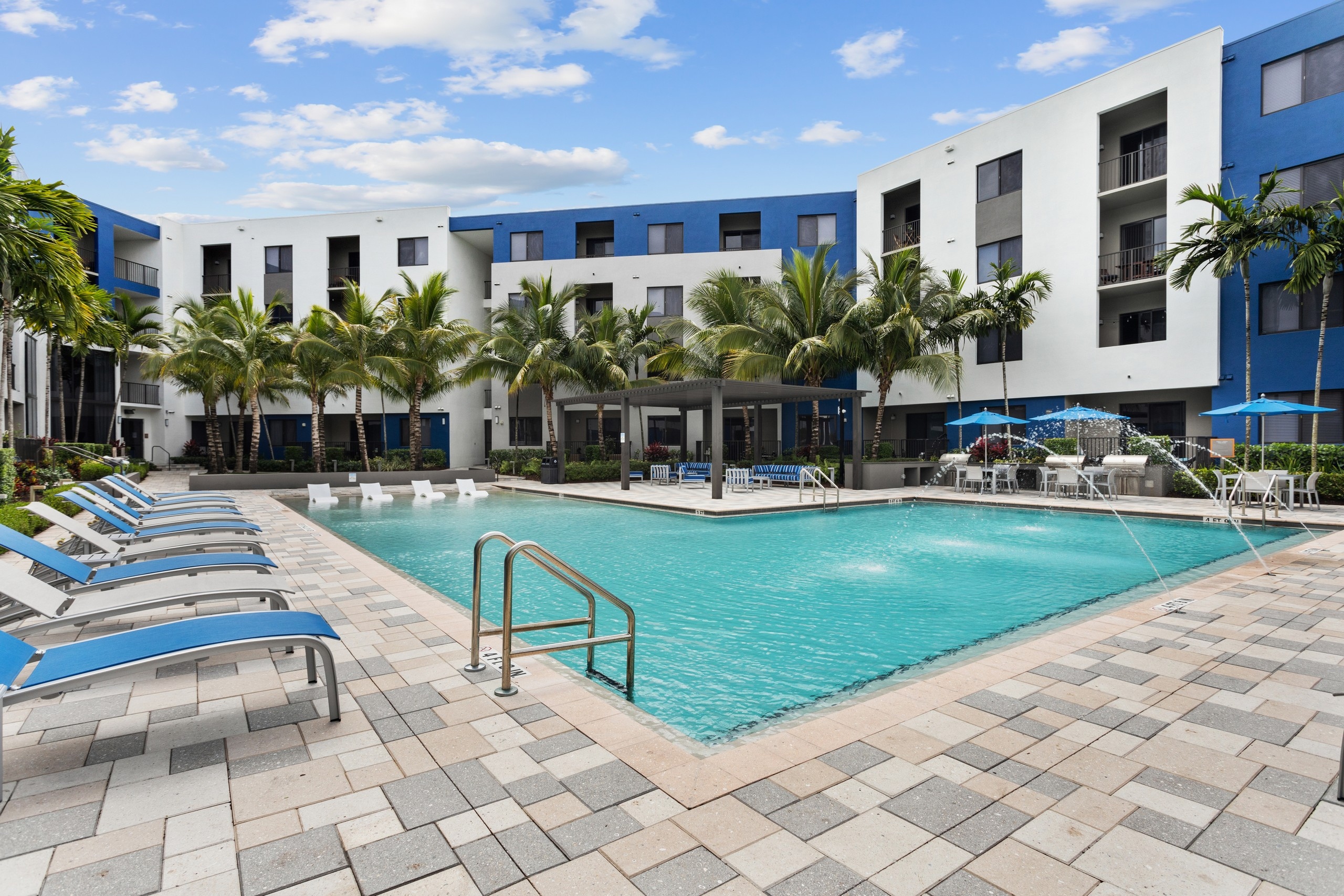 AMLI 8800 pool with water feature and blue and gray lounge chairs a pergola with seating and table and chairs with umbrellas 