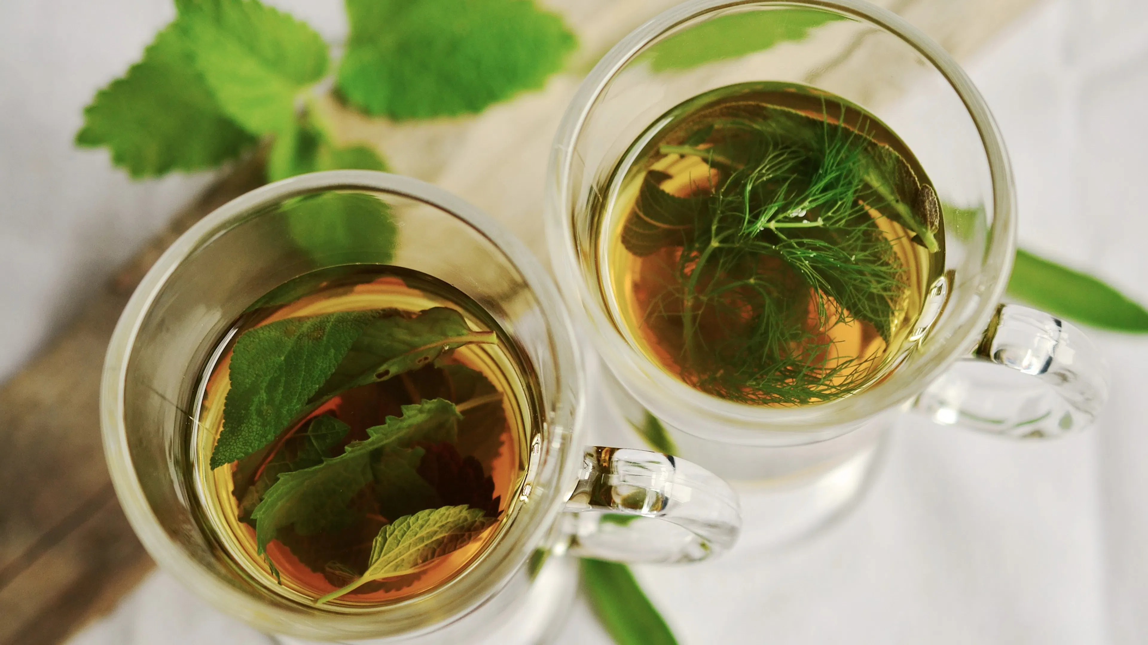 Two glass cups with herbal mint tea set upon a white tablecloth