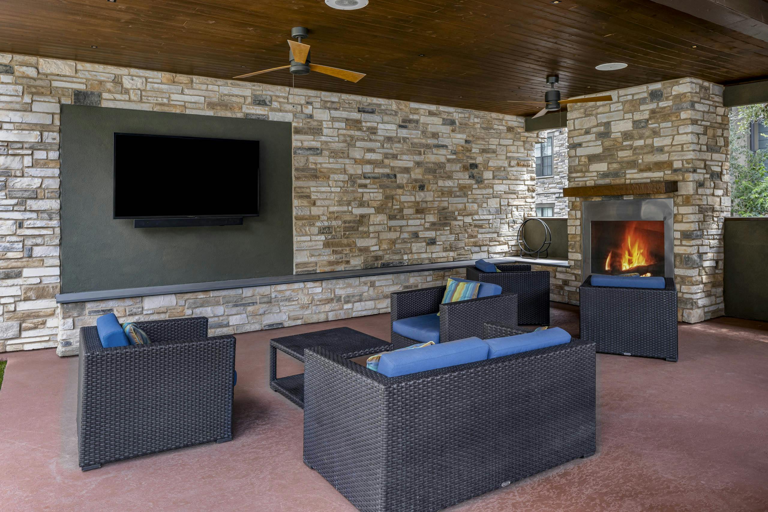 AMLI Covered Bridge cabana with brown wicker seating and blue cushions surrounded by stacked stone walls and fireplace and TV